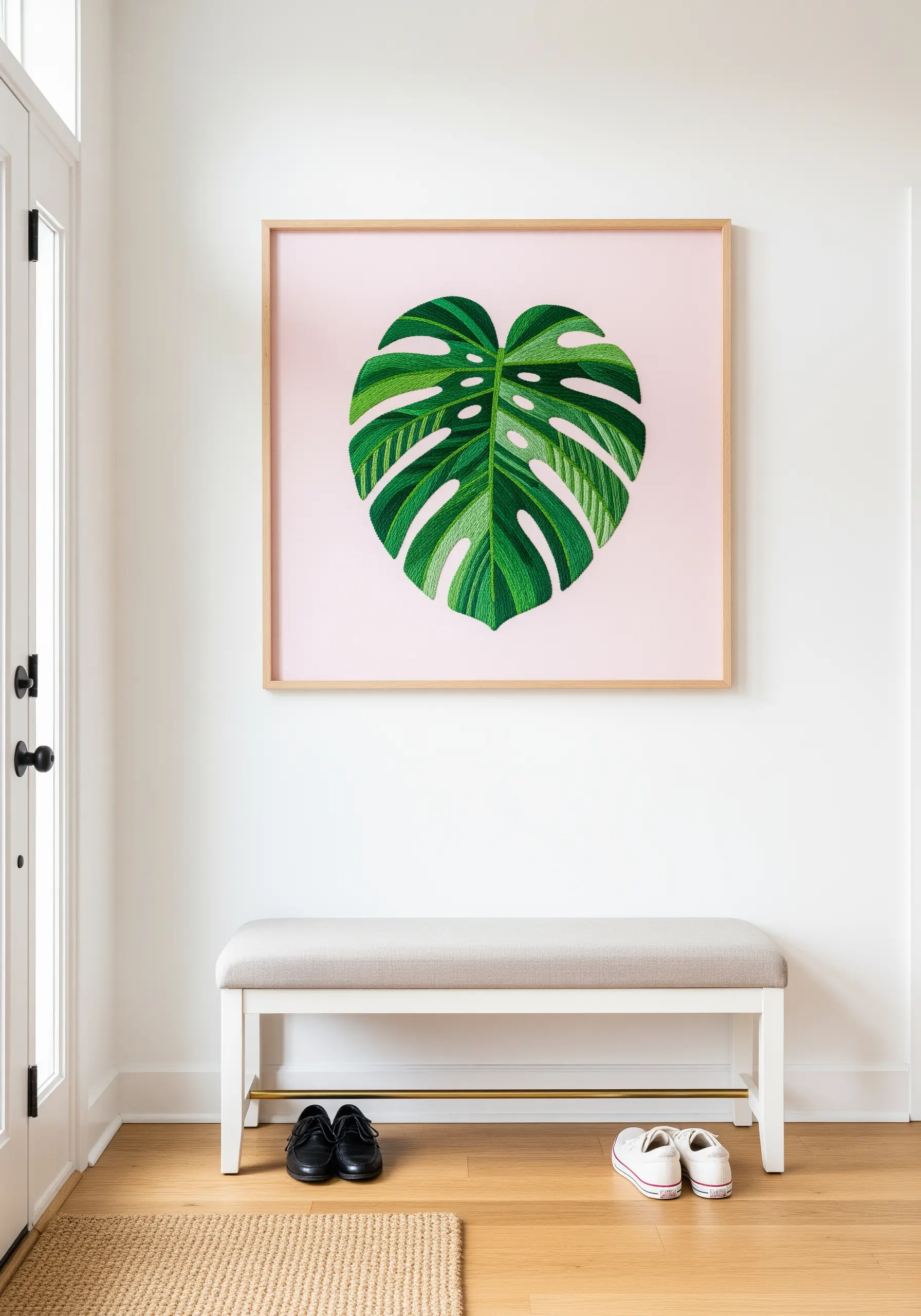A large, realistically embroidered monstera leaf on a solid pink background, framed in light wood.