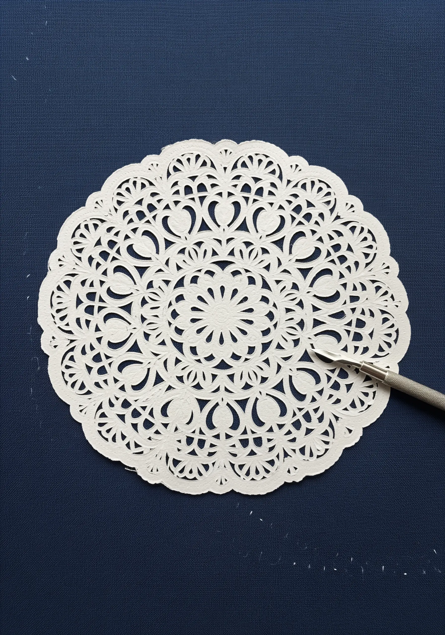An intricate white paper doily on dark blue fabric, serving as a template for an embroidery design.