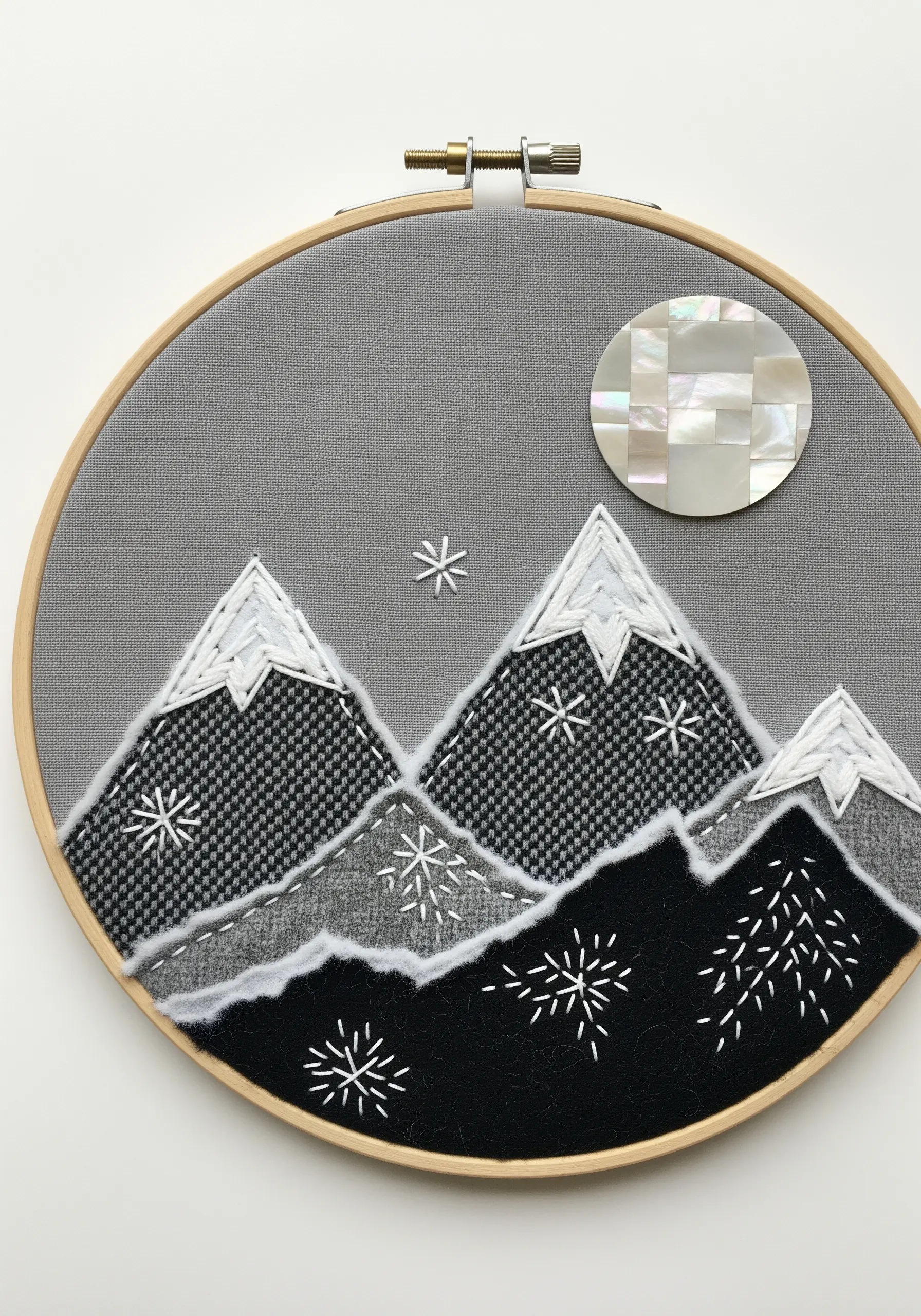 Minimalist mountain landscape embroidery using patterned and felt fabrics with a shell moon.