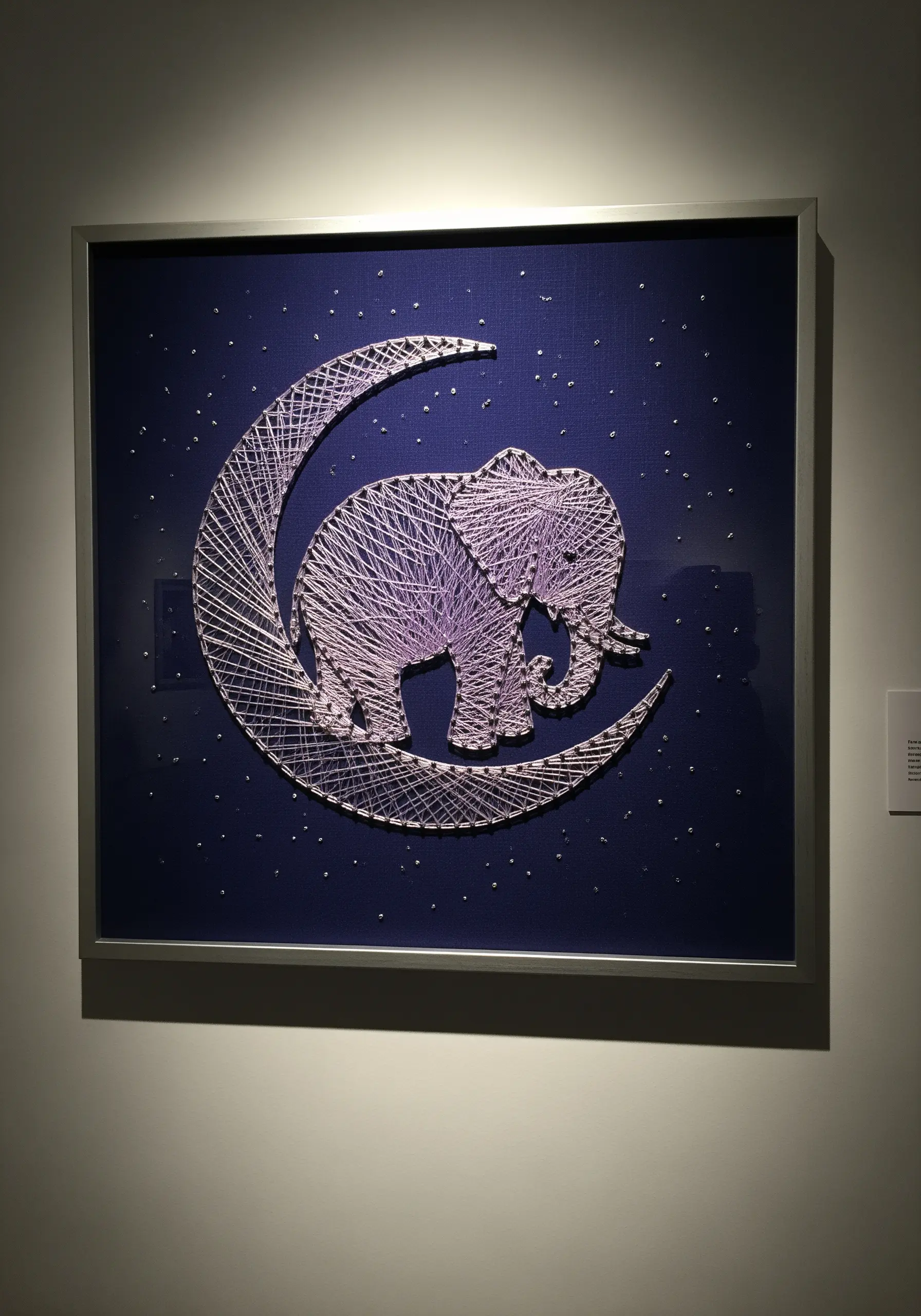 Monochromatic embroidery of an elephant on a crescent moon against a dark blue background.