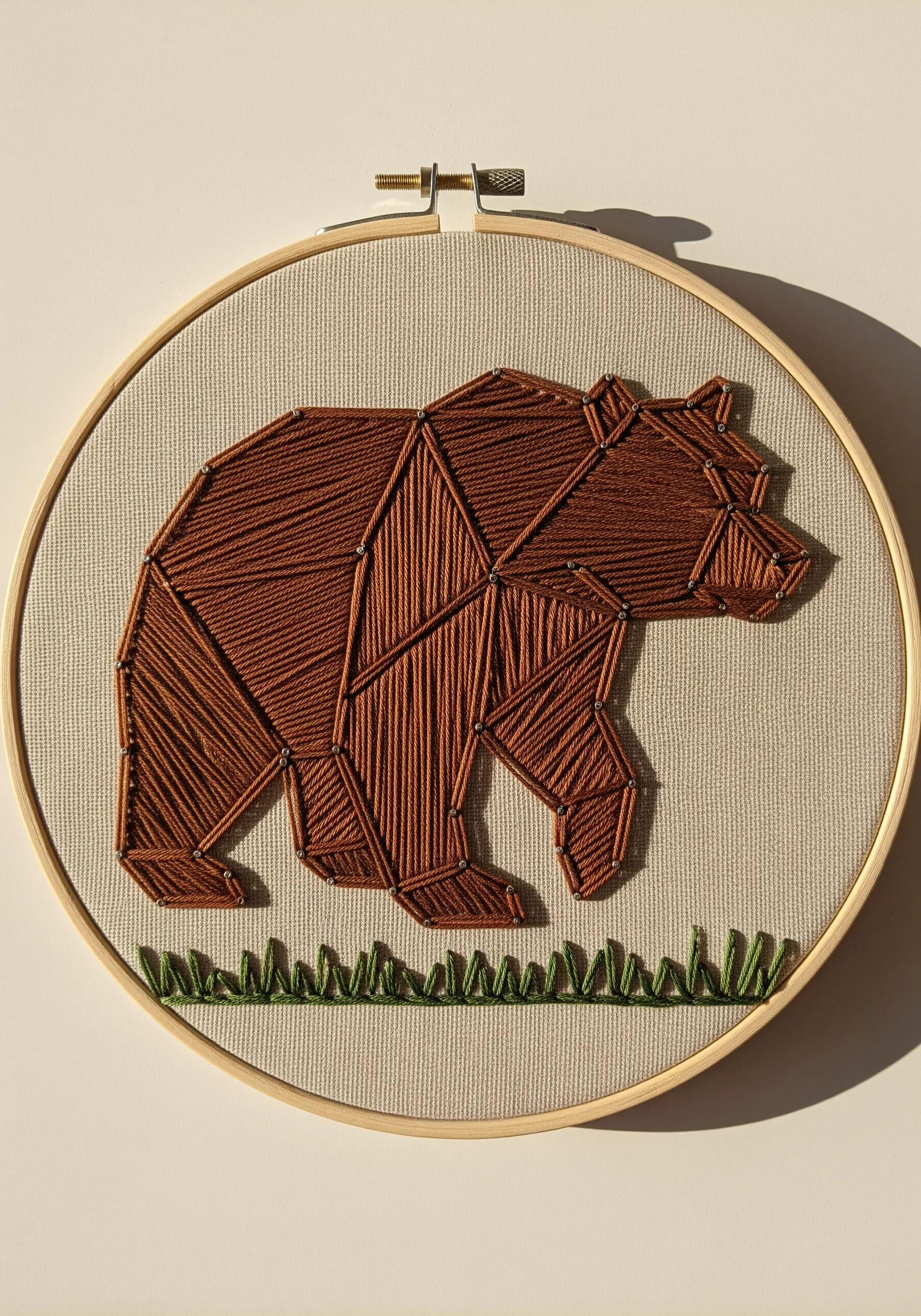 A geometric bear embroidered in brown, with varying stitch directions to create faceted light effects.