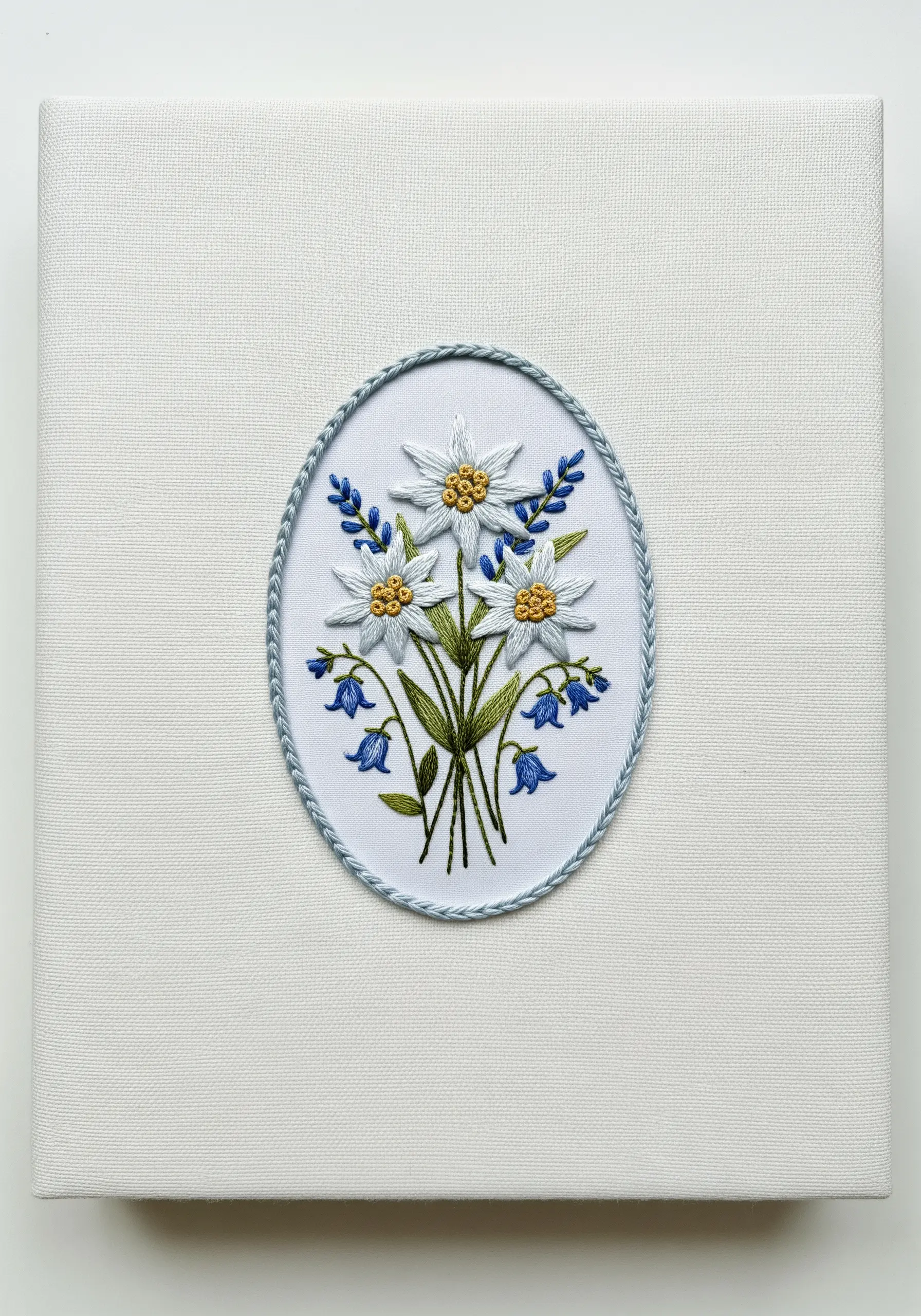 An embroidered bouquet of edelweiss and bluebells inside a decorative oval border.