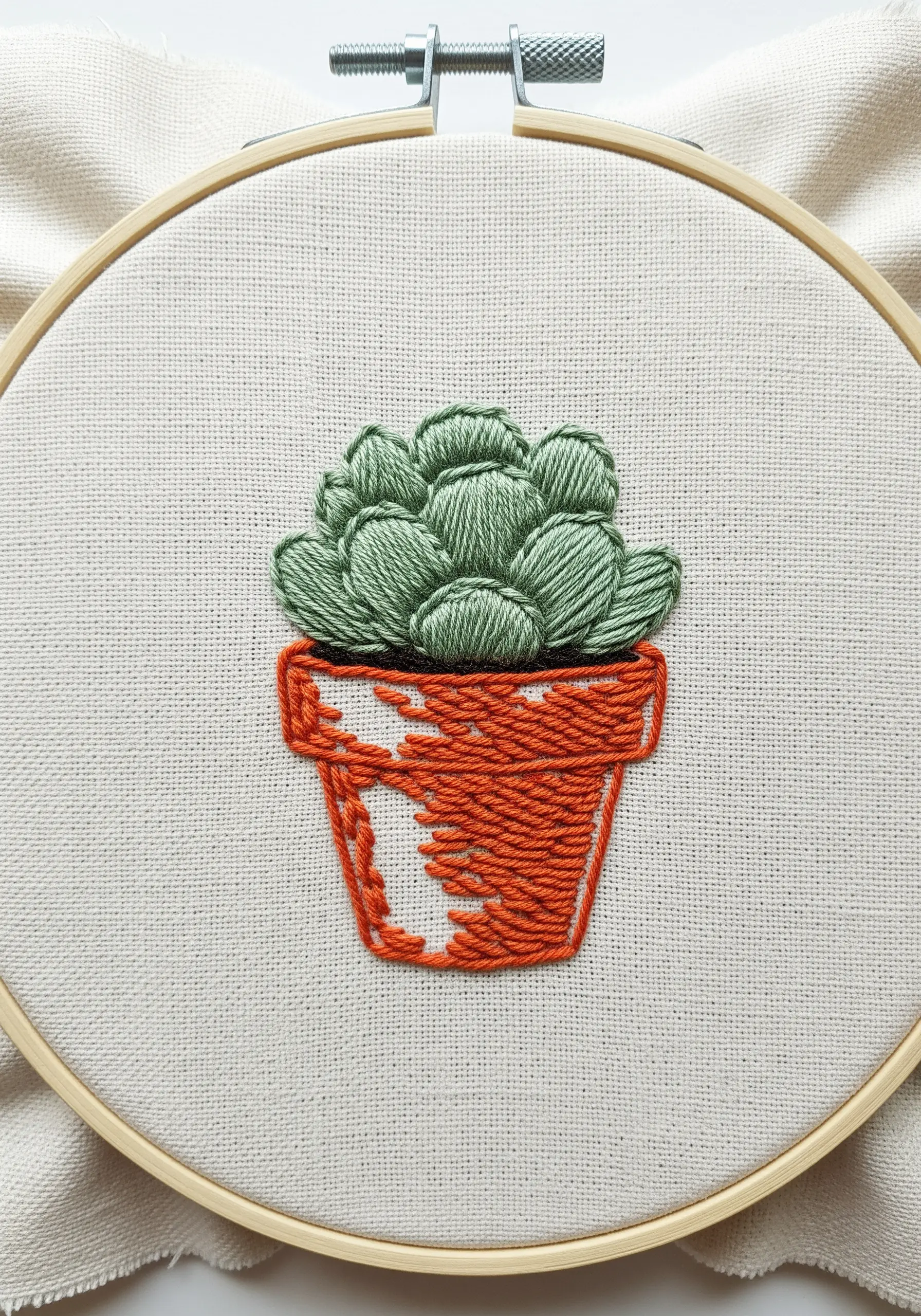A potted succulent with textured orange thread and green satin stitch leaves.