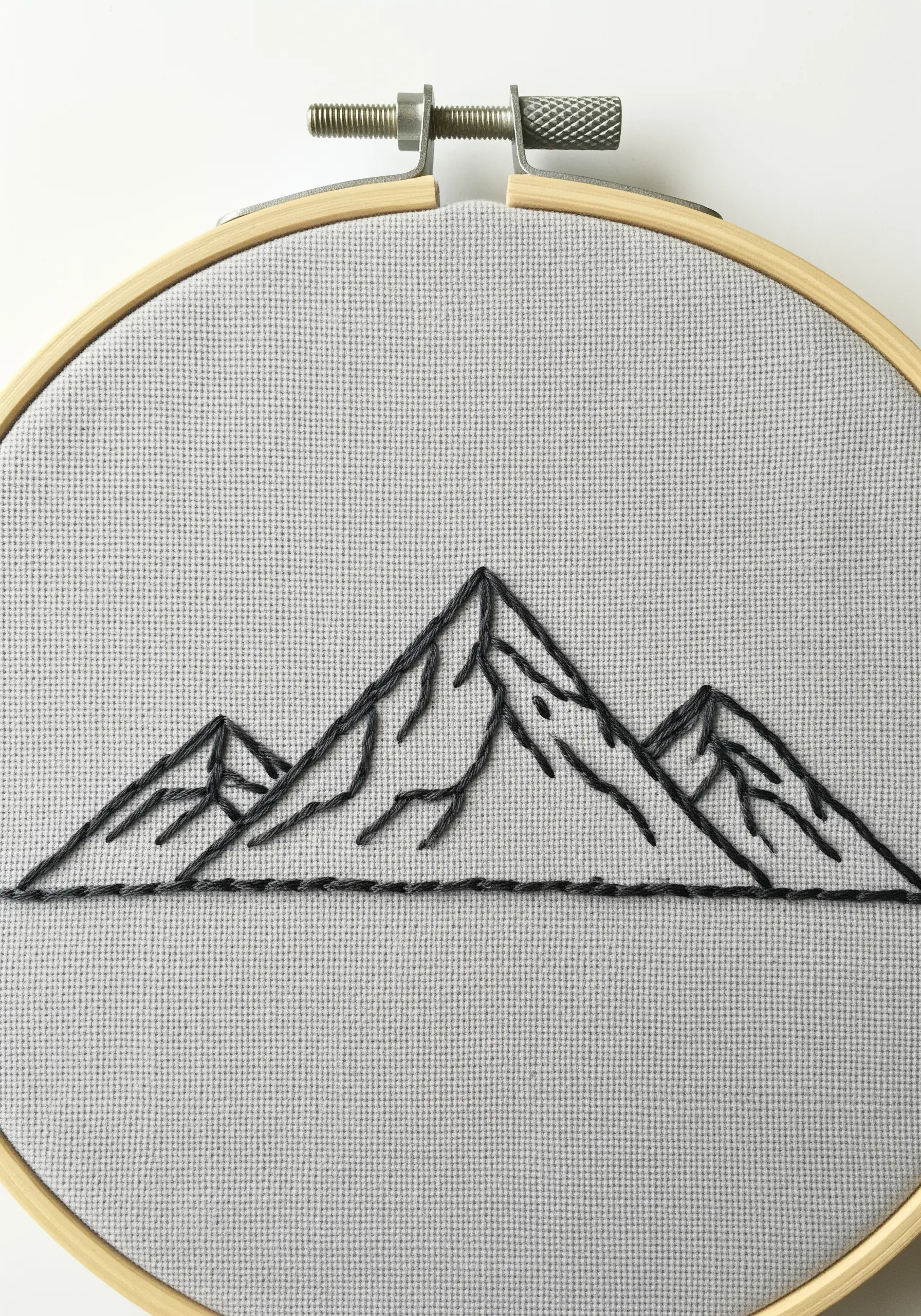 Minimalist line art embroidery of three mountain peaks in a hoop.