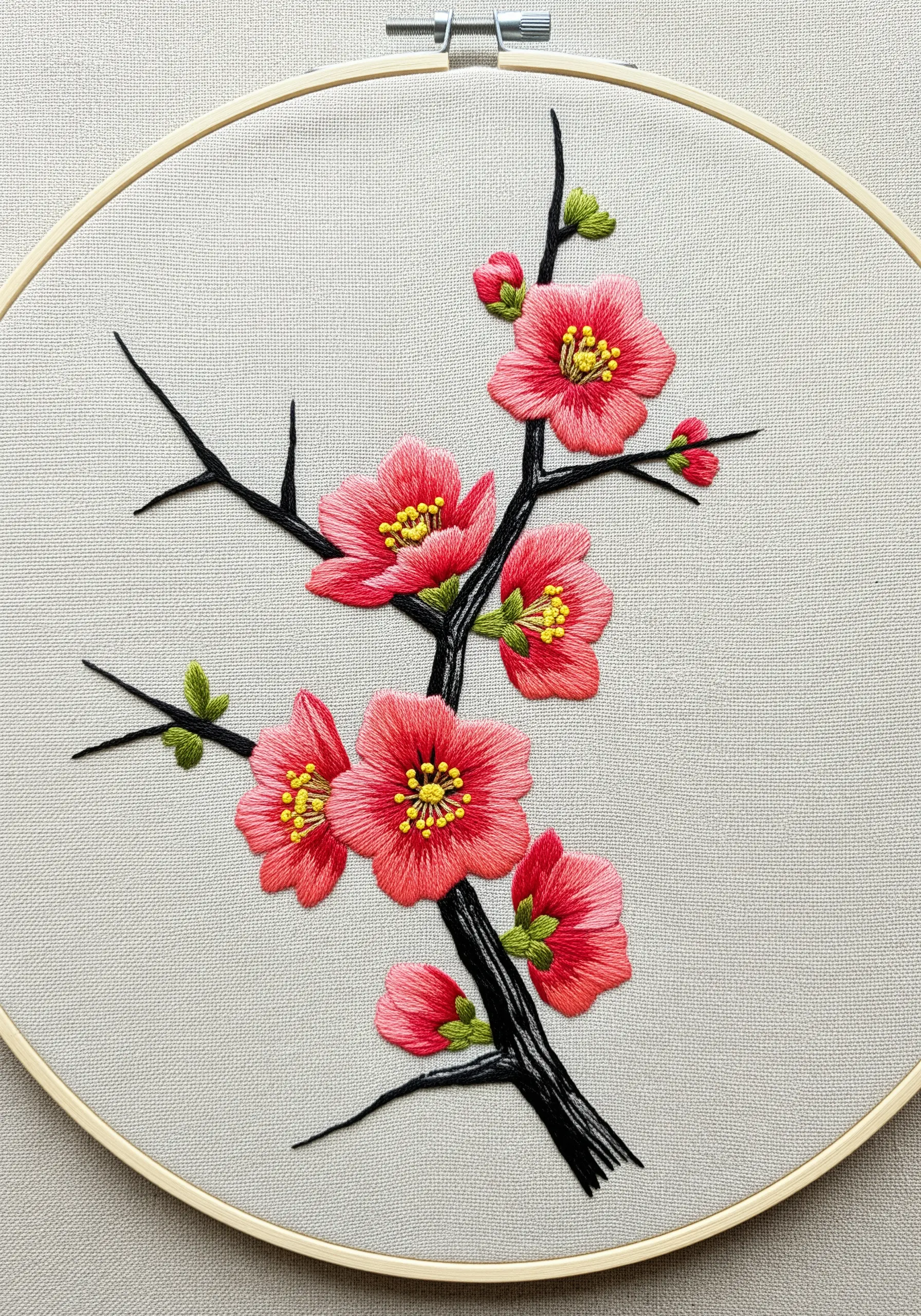 Thread-painted Japanese quince blossoms in vibrant coral on a neutral fabric background.