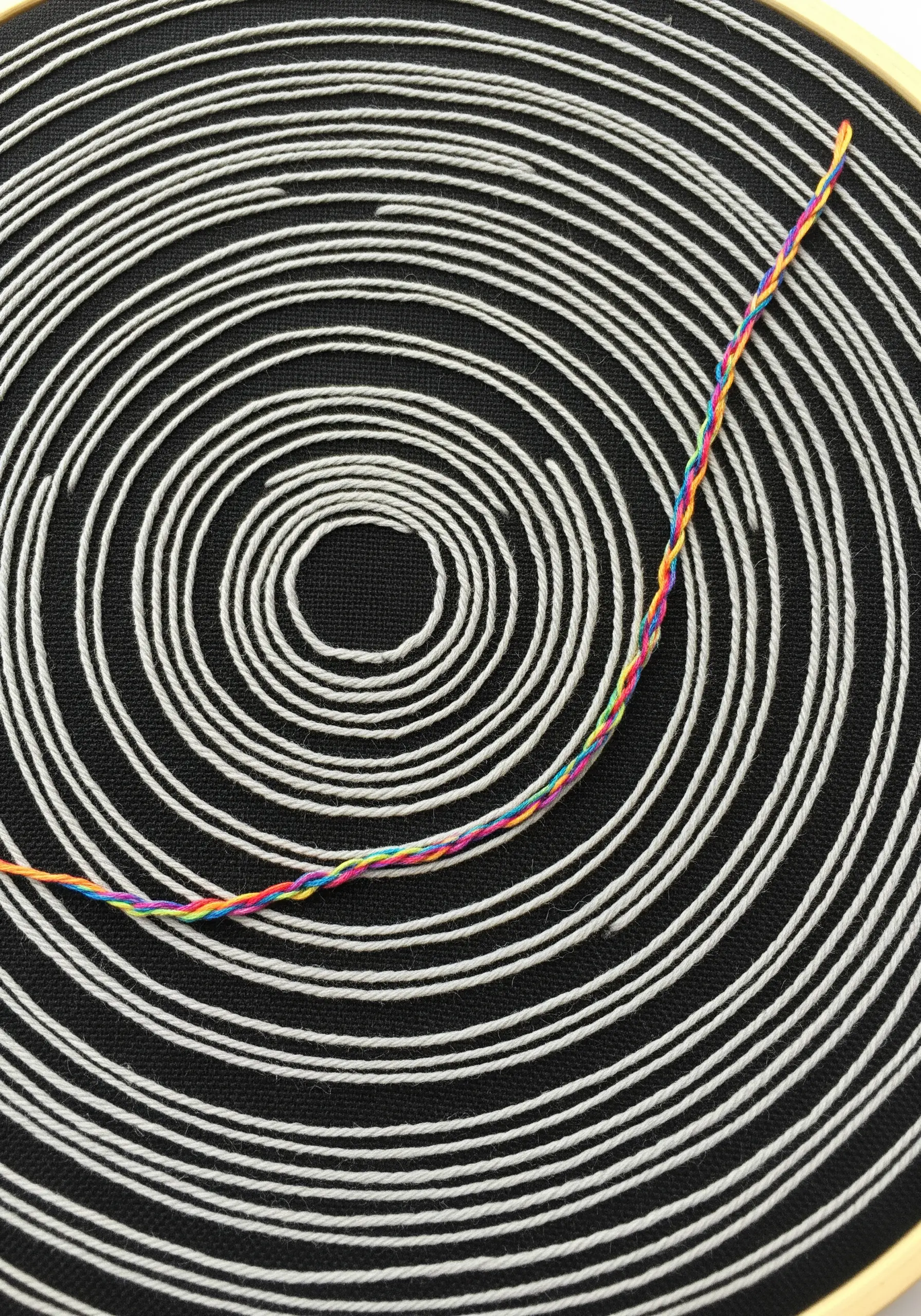 Concentric white stitched circles on black fabric with a single rainbow twisted thread.