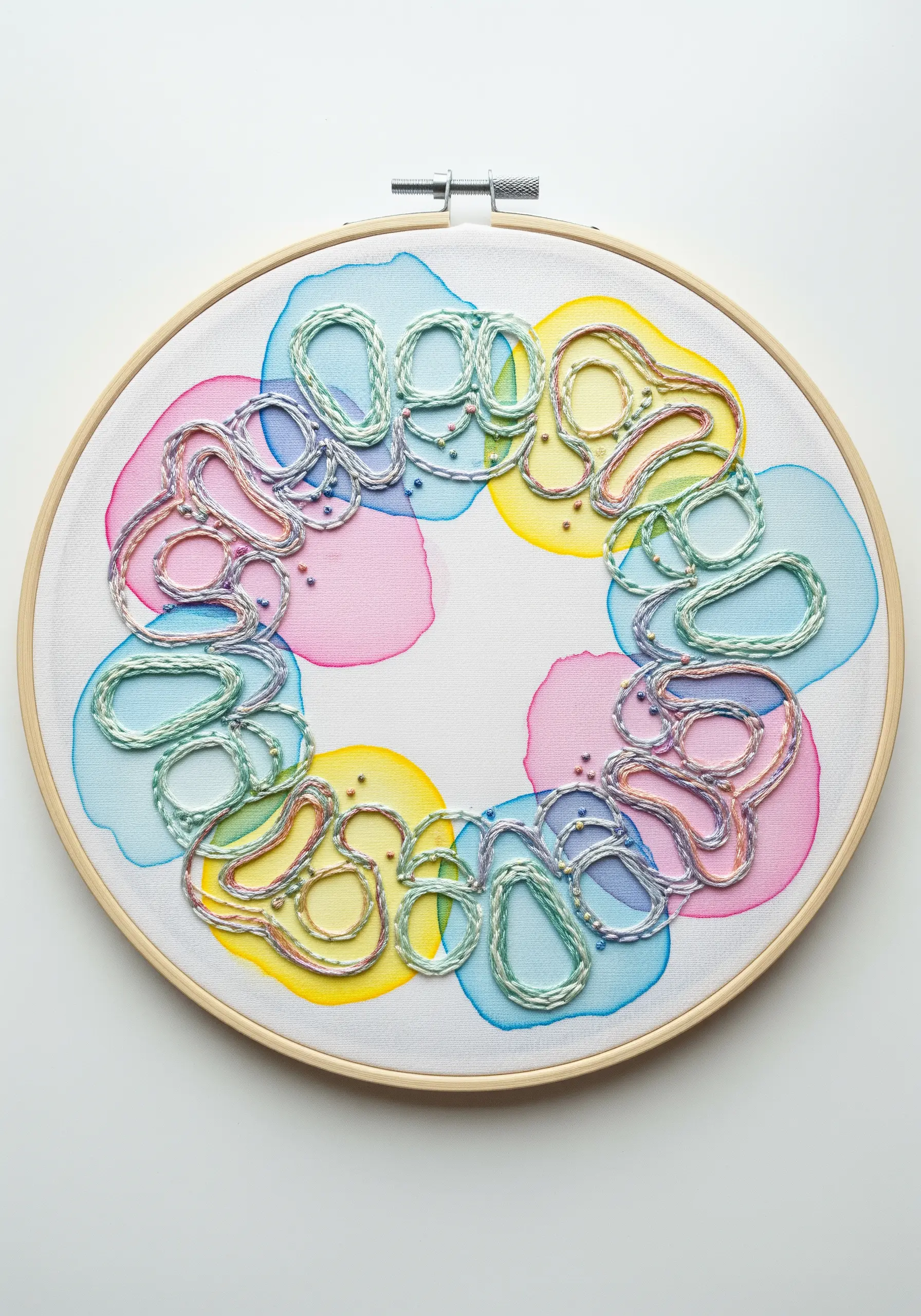 Abstract hoop art with watercolor splotches in pink, blue, and yellow, overlaid with embroidery.