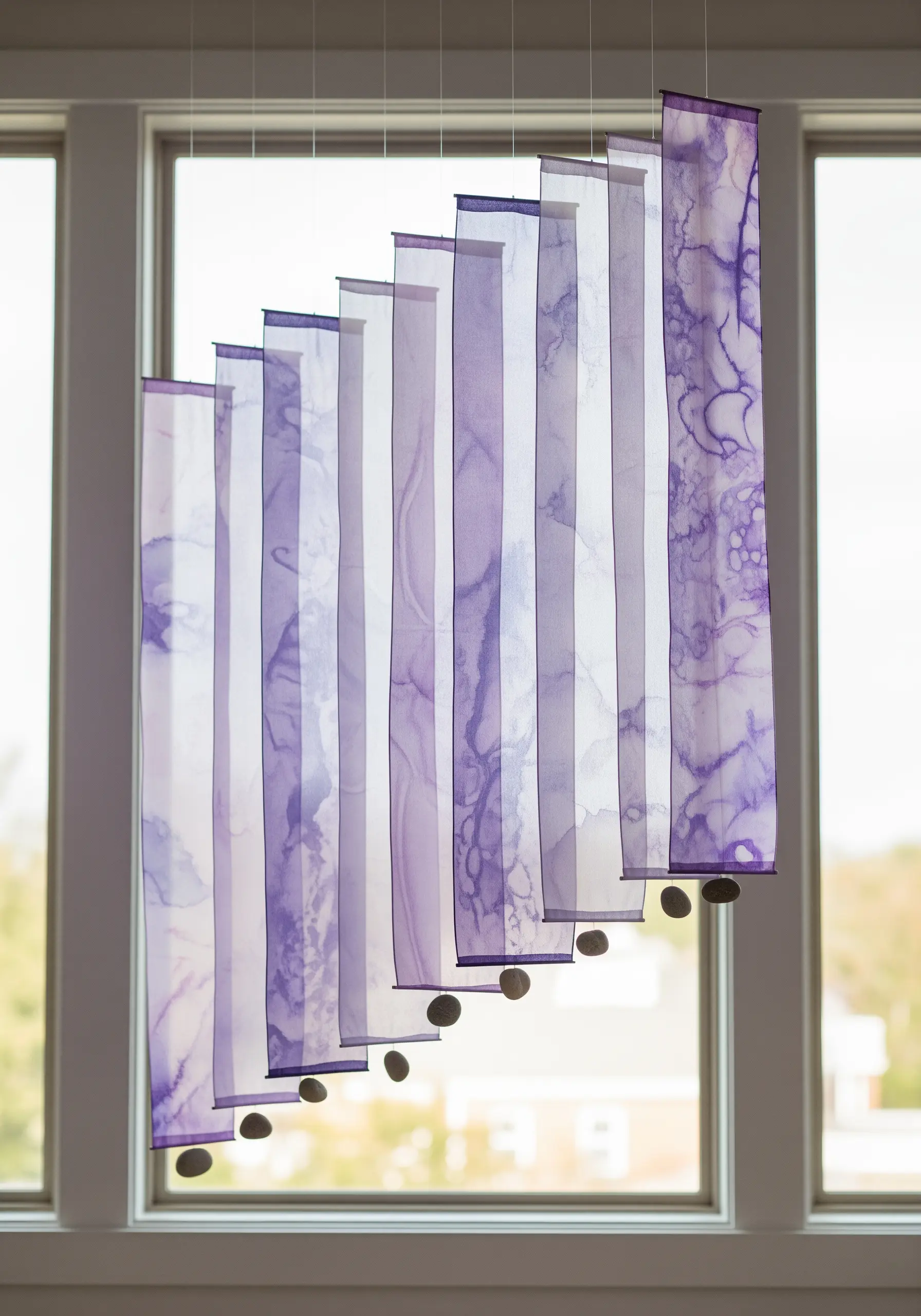 Sheer purple fabric panels with watercolor-like stains, hanging in layers in a window.