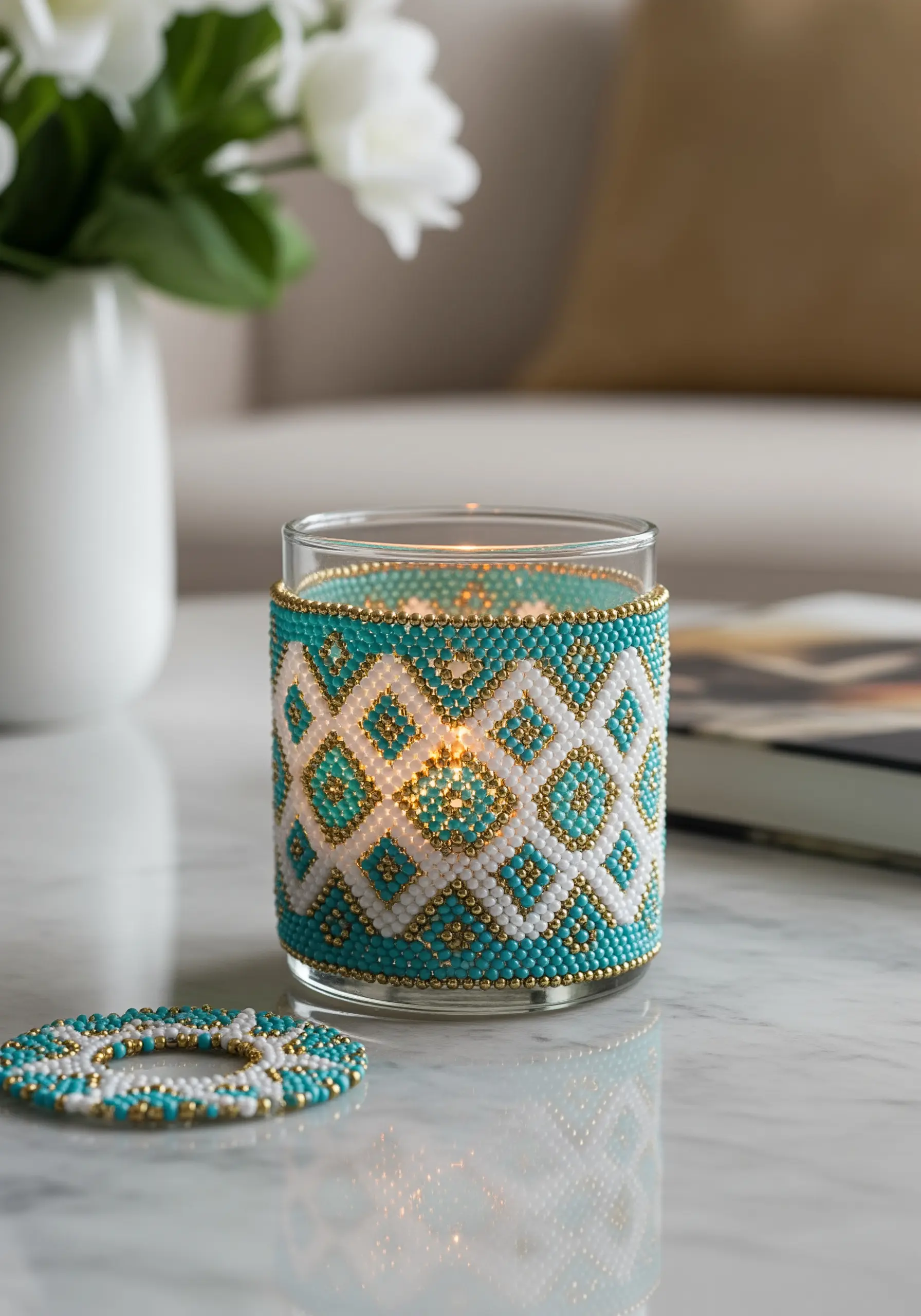 A glass candle holder wrapped in an intricate woven sleeve of turquoise, white, and gold beads.