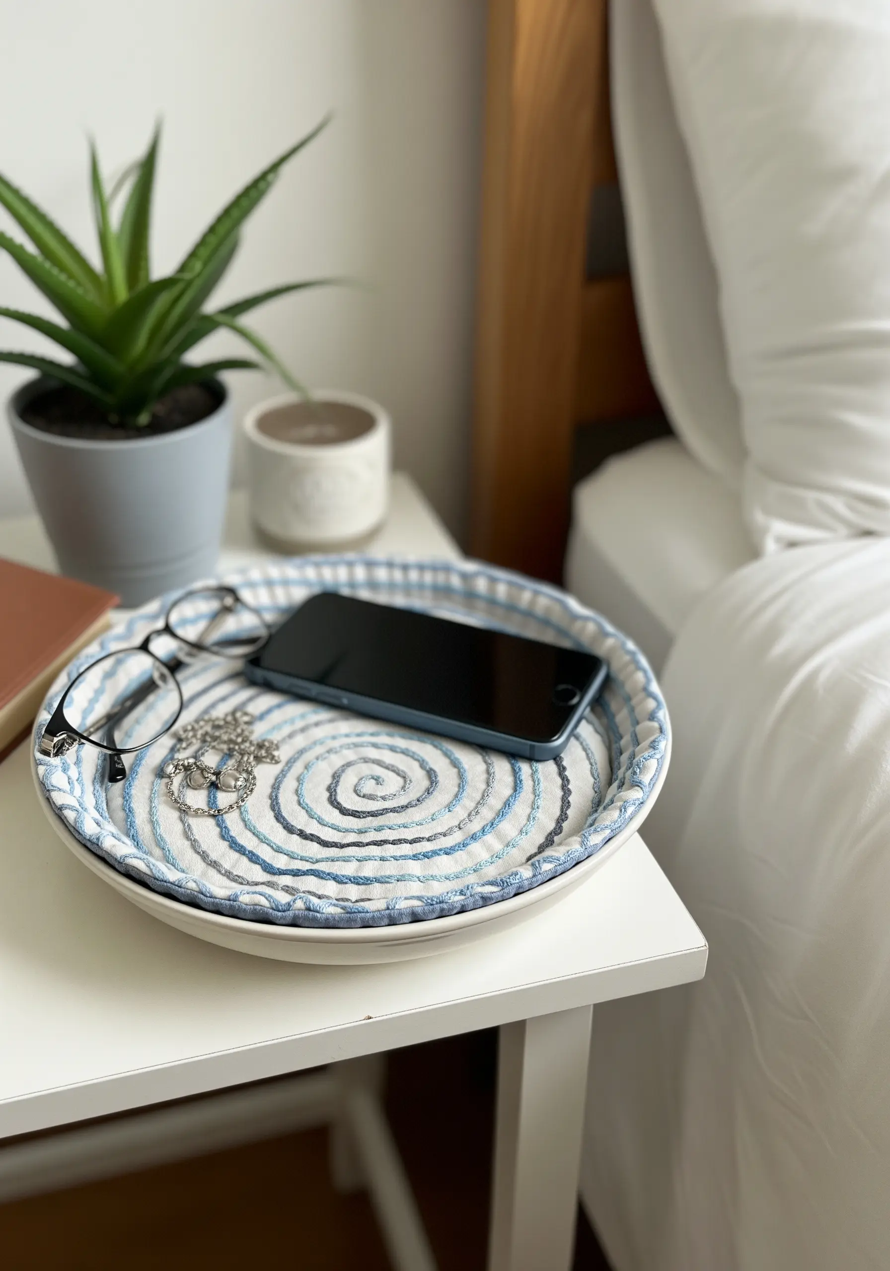 A coiled rope tray with blue and white fabric, holding a phone and glasses.