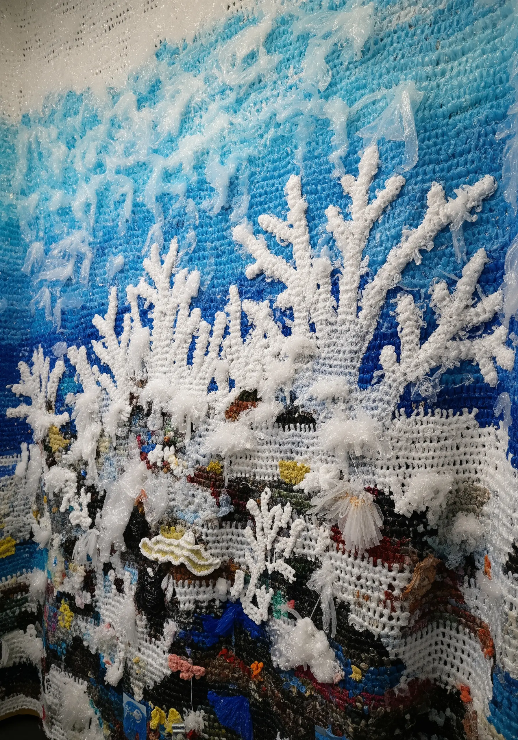 A detailed textile artwork of a coral reef incorporating recycled plastic and other materials.