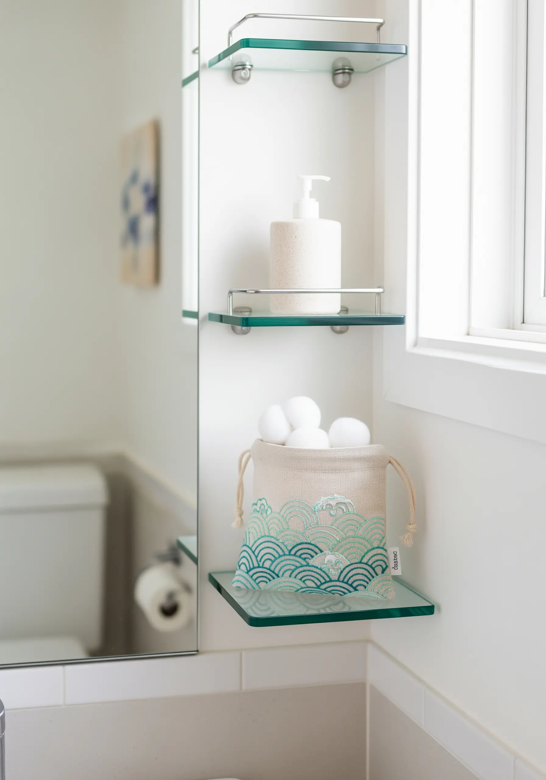 A linen drawstring pouch on a bathroom shelf, embroidered with a teal wave pattern.