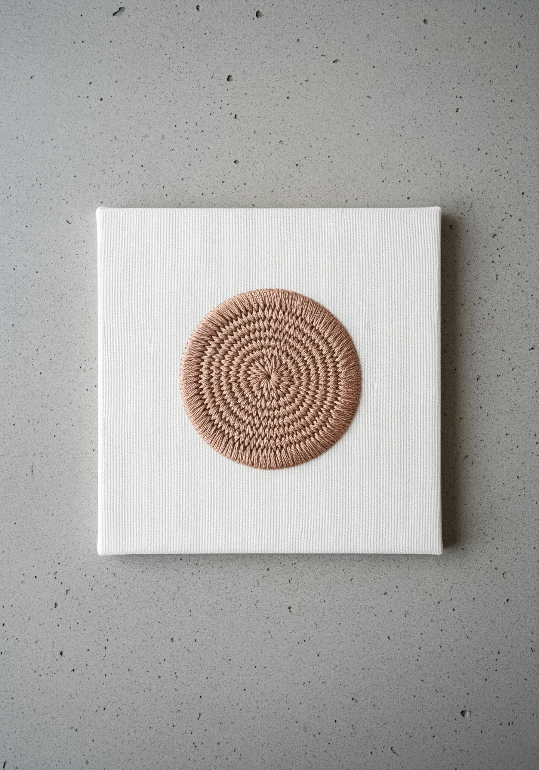 A perfectly woven circle in beige thread on a square white canvas.