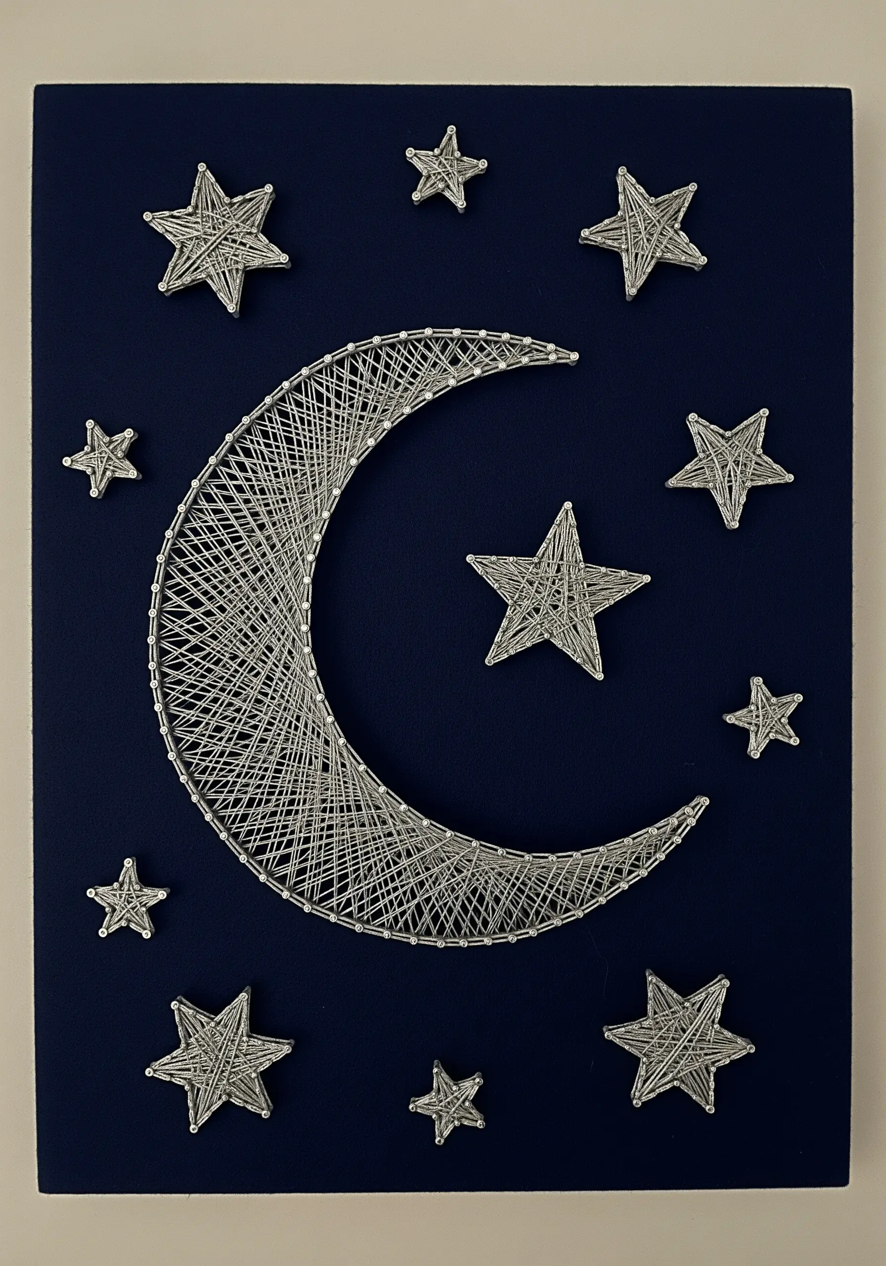 A crescent moon and stars embroidered with layered silver metallic thread on a dark blue background.