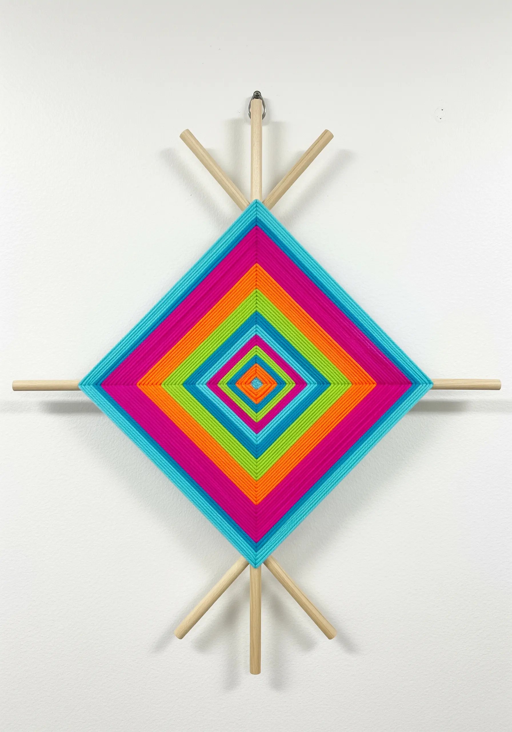 A brightly colored Ojo de Dios yarn weaving with concentric diamond shapes.