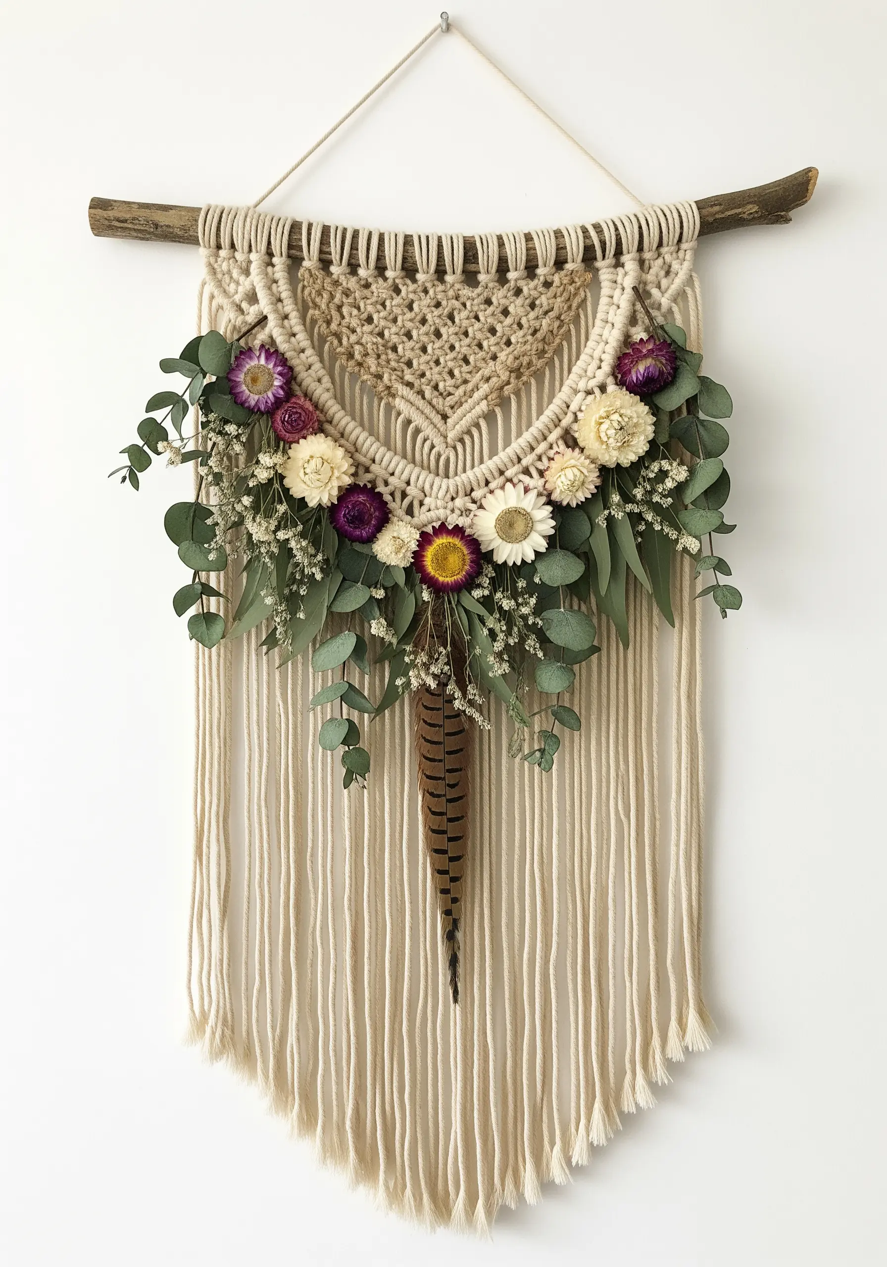 A neutral macrame wall hanging adorned with dried flowers, eucalyptus, and a feather.