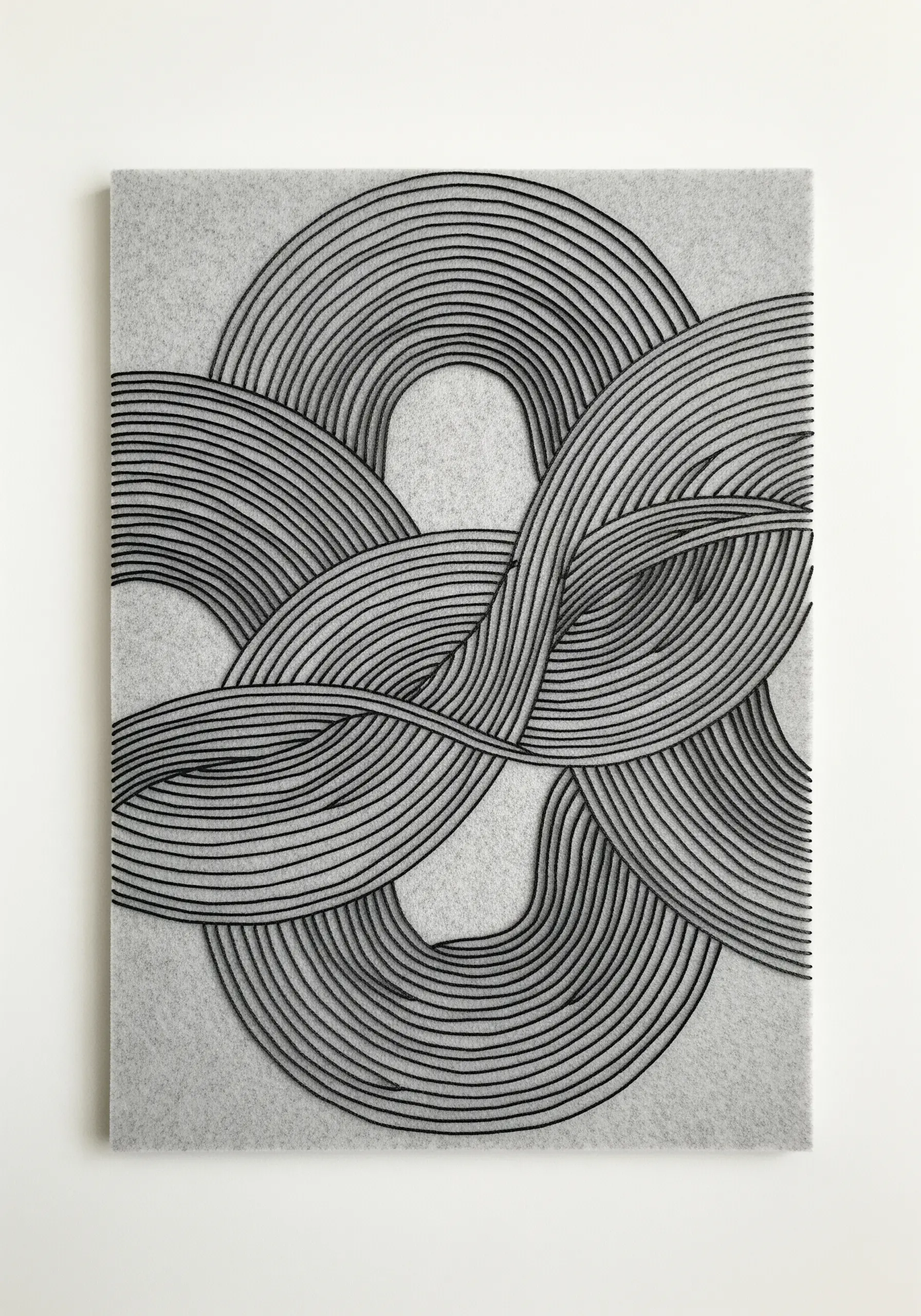 An abstract artwork of densely couched black cord forming an intricate, interwoven knot on grey felt.