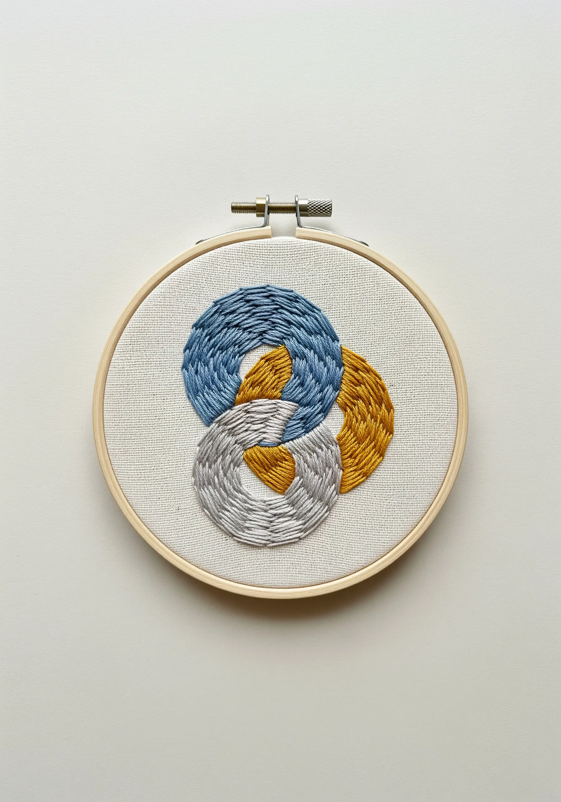 Three interlocking rings in blue, yellow, and gray with directional satin stitches.