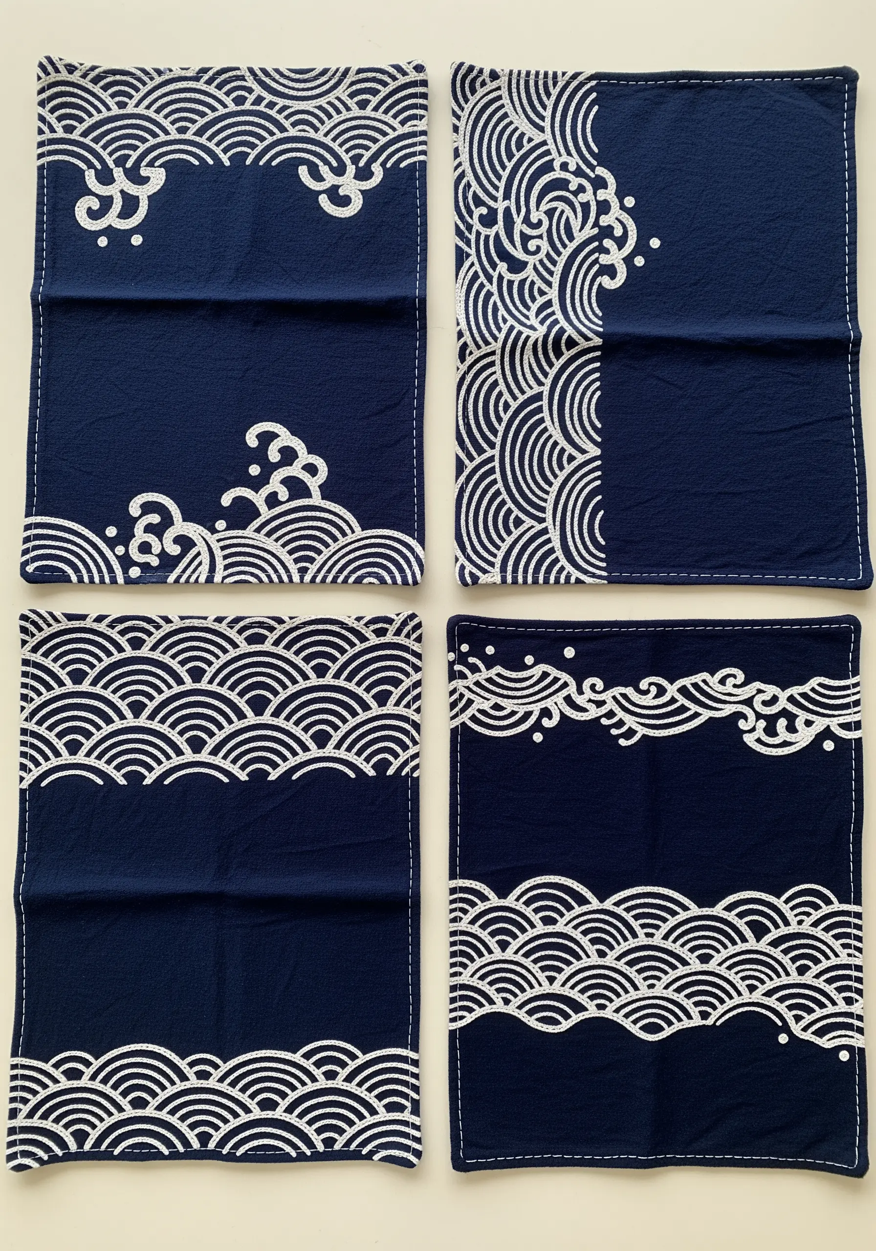Four indigo blue napkins with minimalist white embroidery depicting Japanese-style ocean waves.