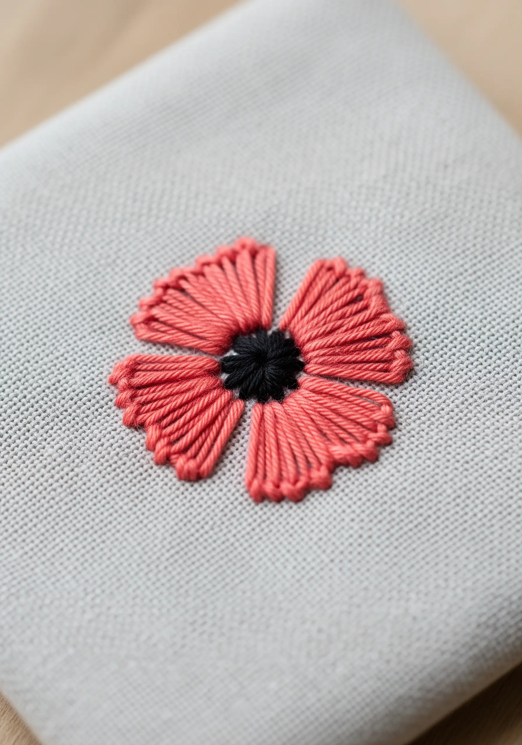 A red poppy with four woven wheel petals and a black French knot center.