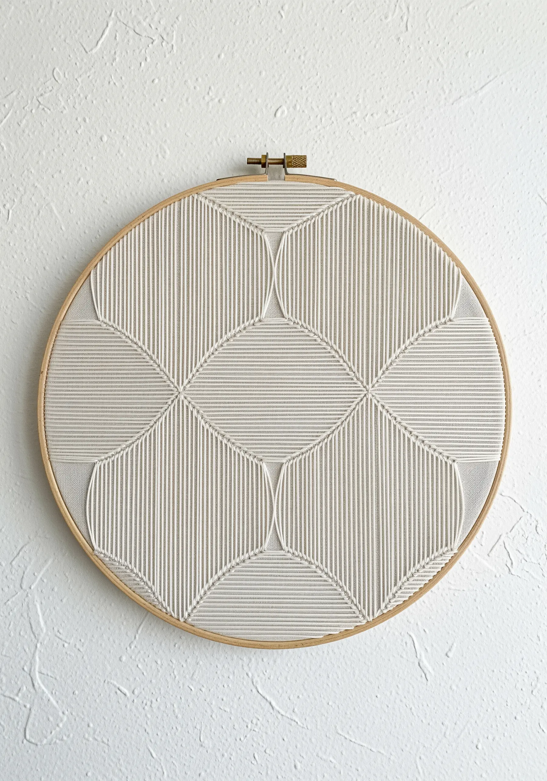 A hoop filled with dense, white-on-white stitches creating a geometric, woven pattern.