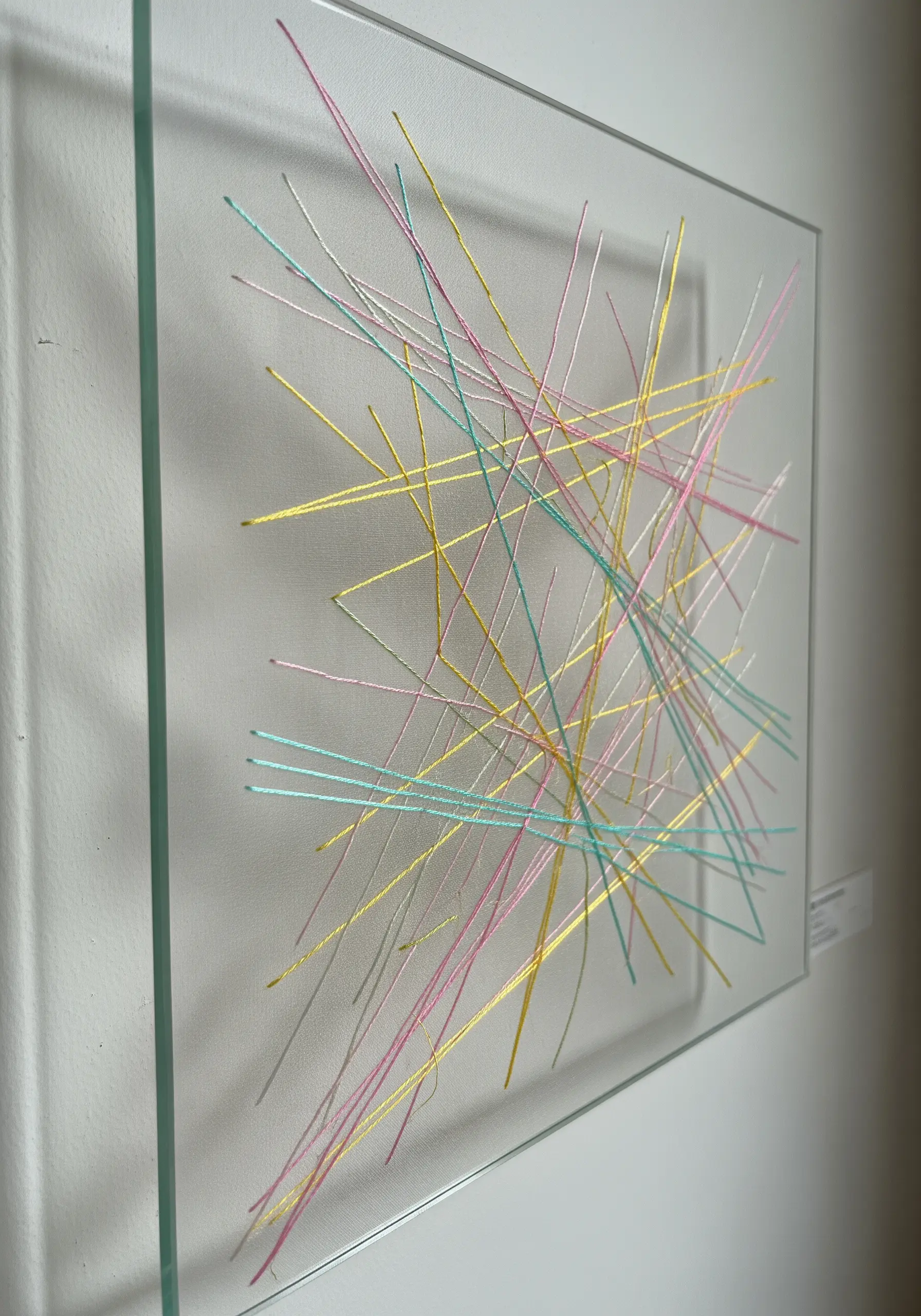 Abstract thread art created by stretching colorful threads across a transparent pane of glass in a frame.