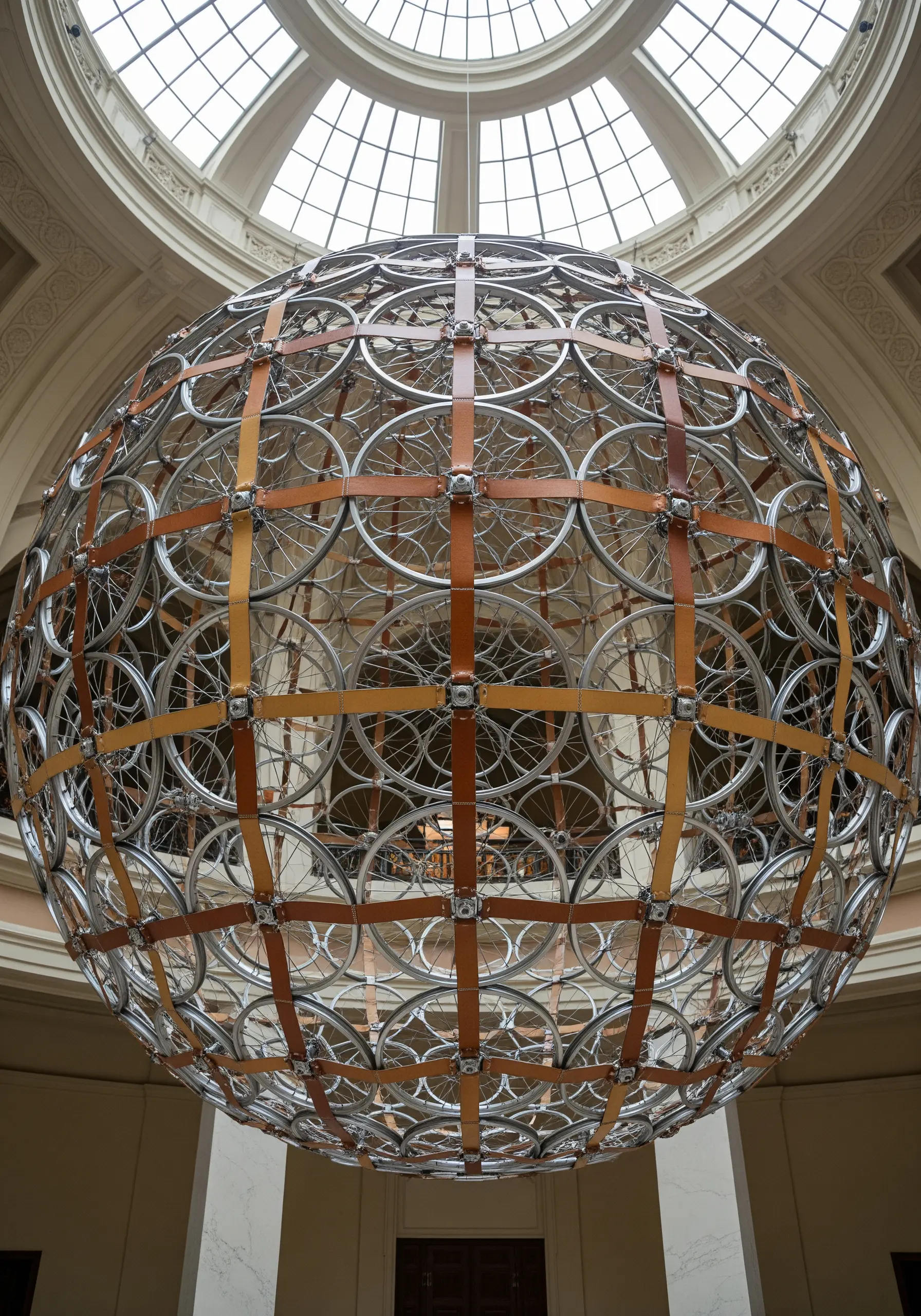 A massive spherical chandelier made from hundreds of bicycle wheel rims bound by leather straps.