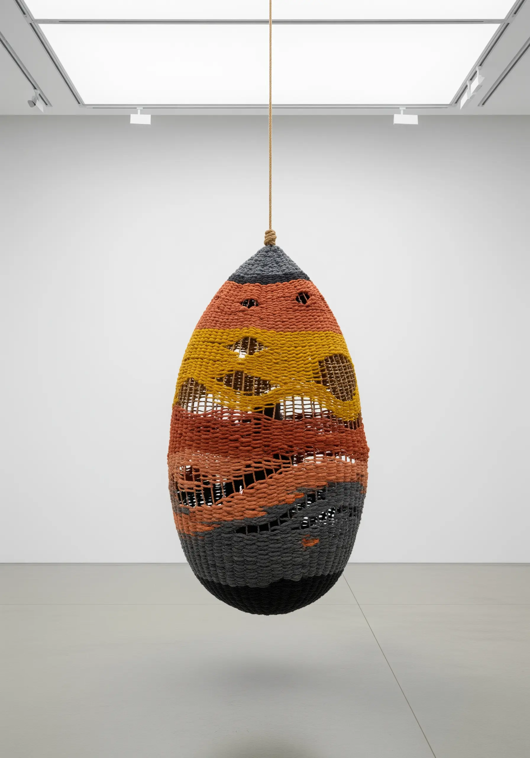 A large, woven hanging sculpture in earthy tones with intentional gaps in the weave.