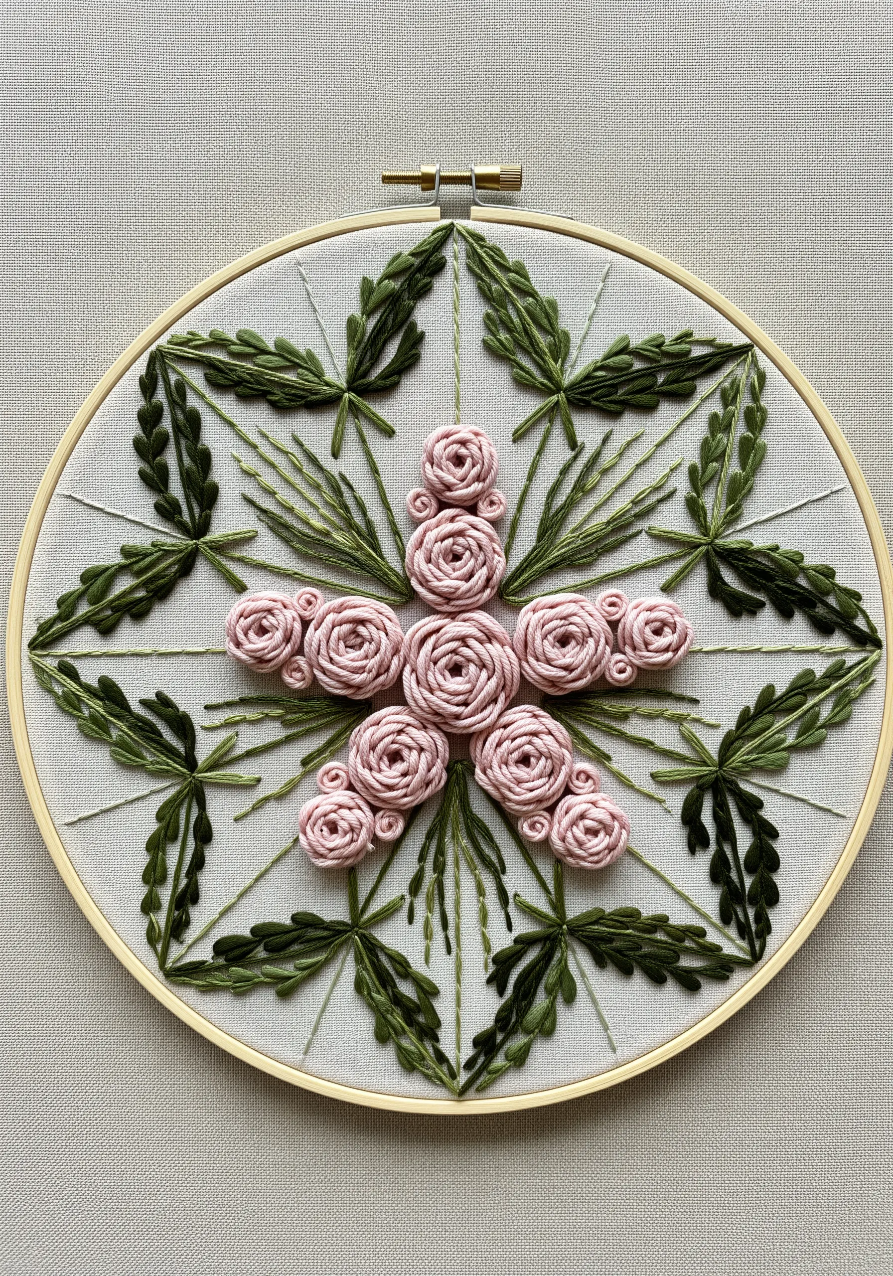 A symmetrical mandala design with a central cluster of pink woven wheel roses and green leaf stitches.