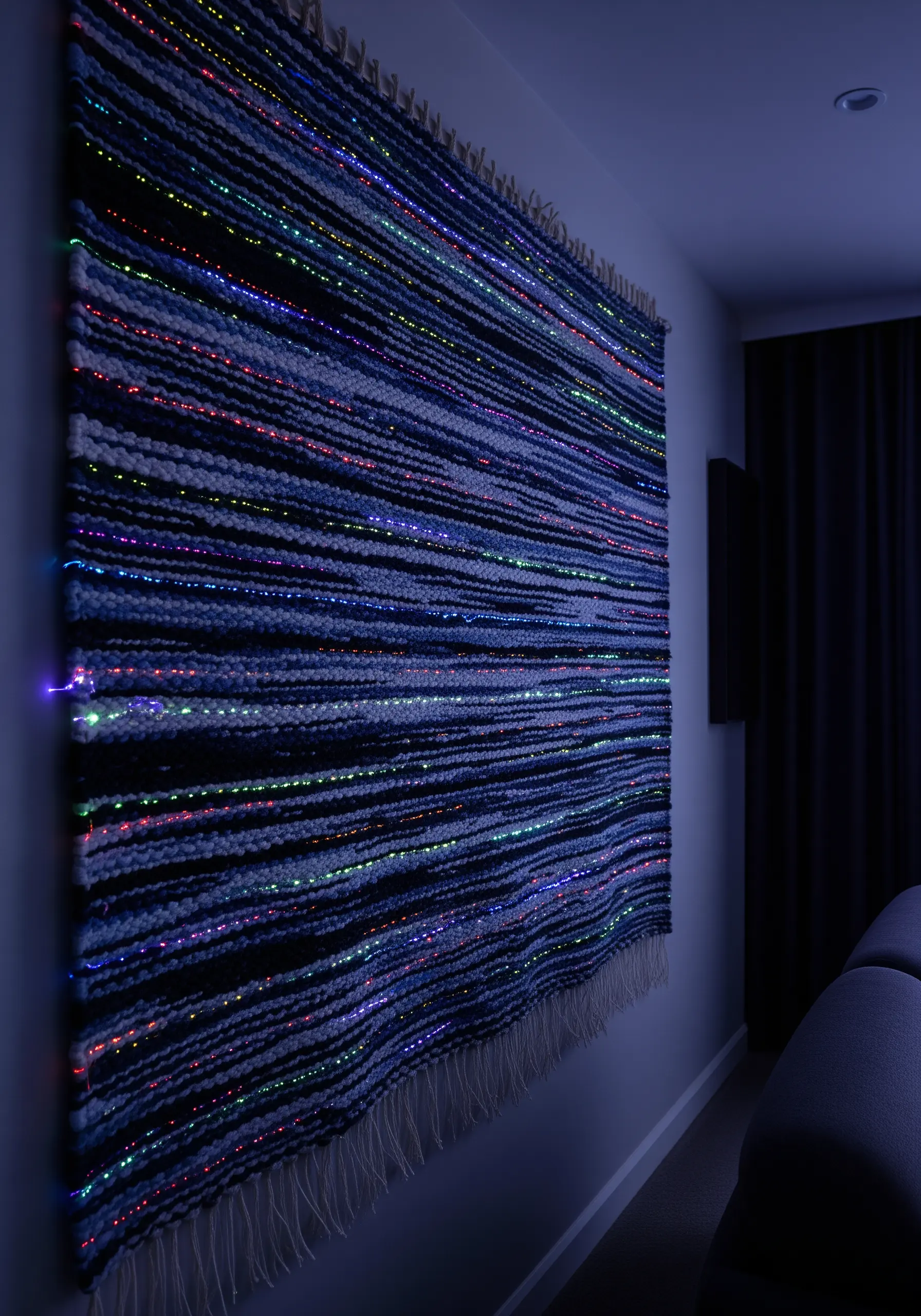 A dark woven wall hanging illuminated from within by colorful fiber optic lights.