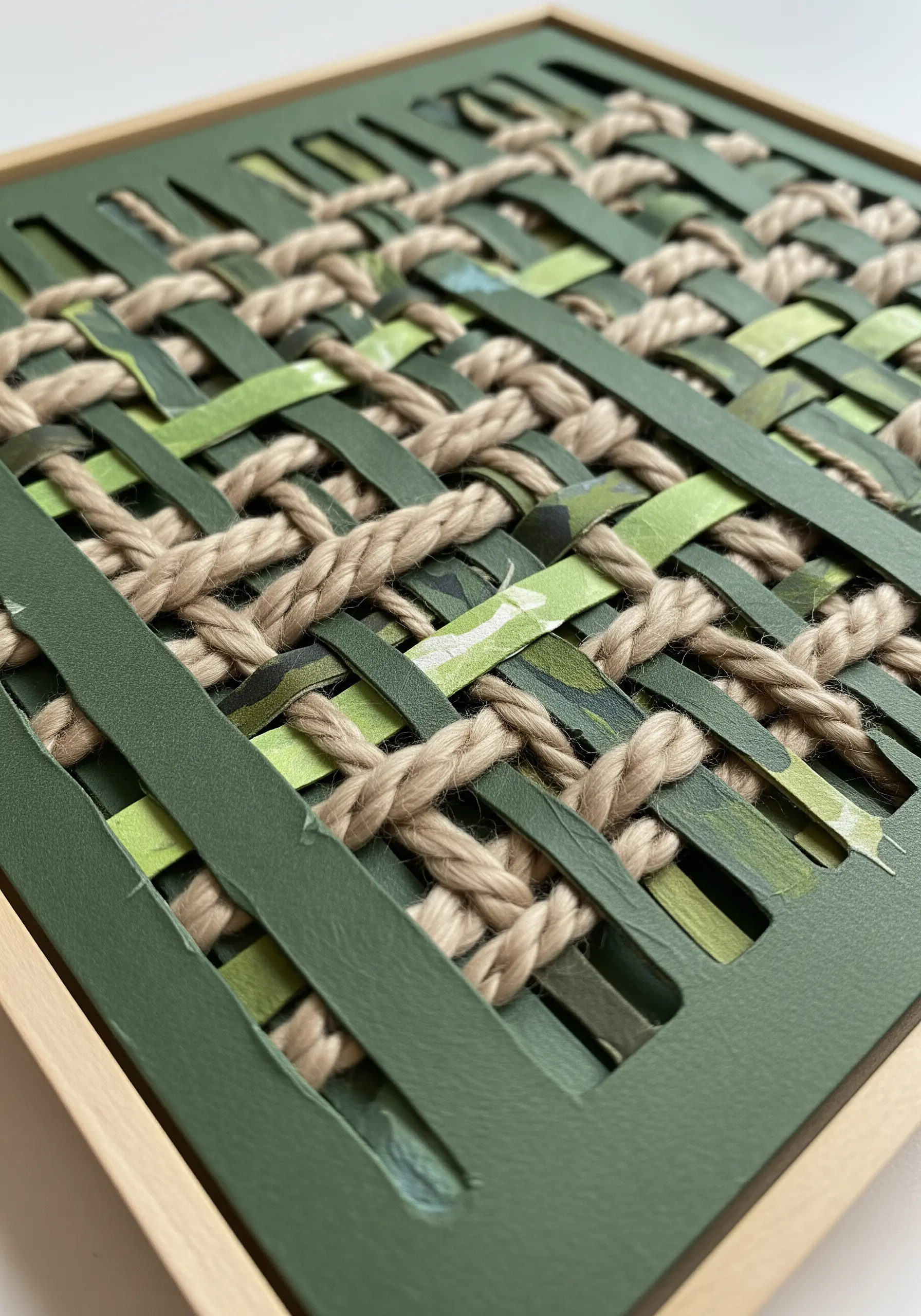 A woven piece combining green paper strips with thick, natural jute rope in a wooden frame.