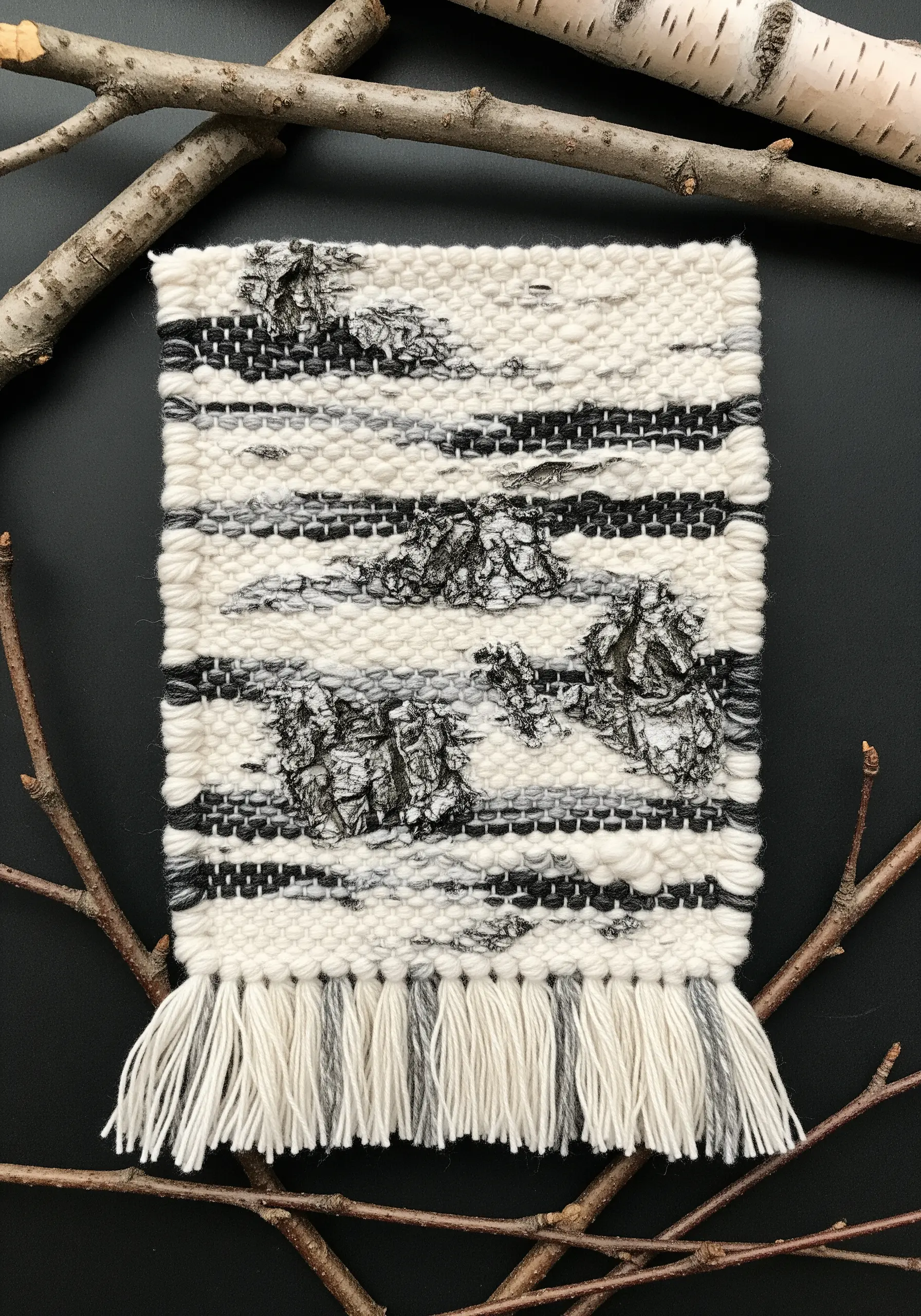 A woven wall hanging in neutral tones with pieces of real birch bark integrated into it.