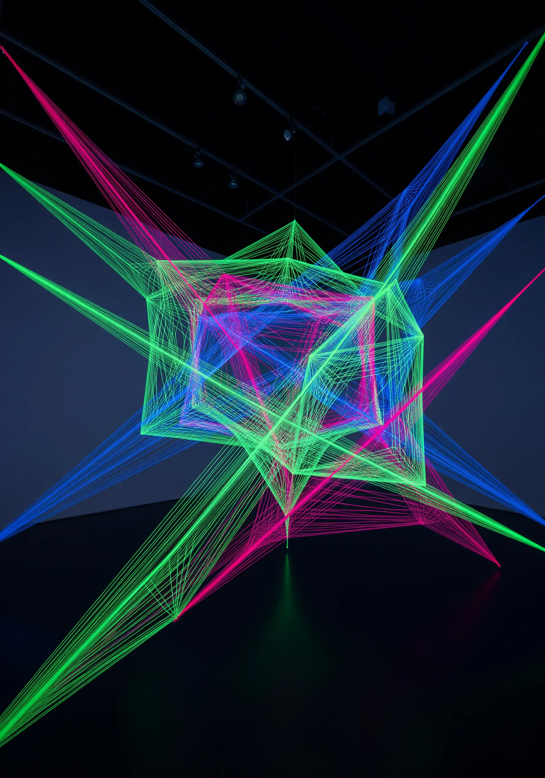 A geometric 3D cube installation made of glowing neon threads in a dark room.