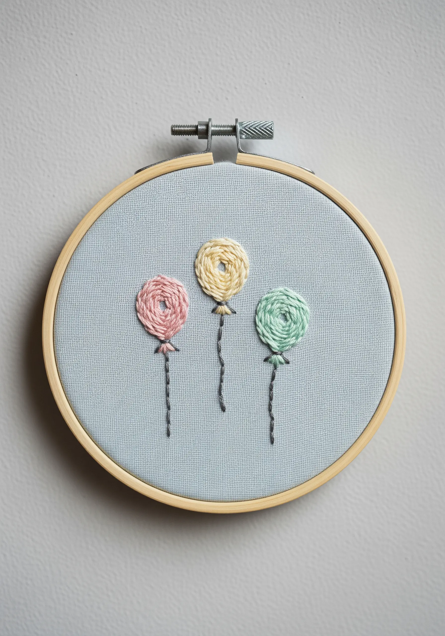 Three pastel-colored woven wheel stitches used as abstract balloons with stitched strings.