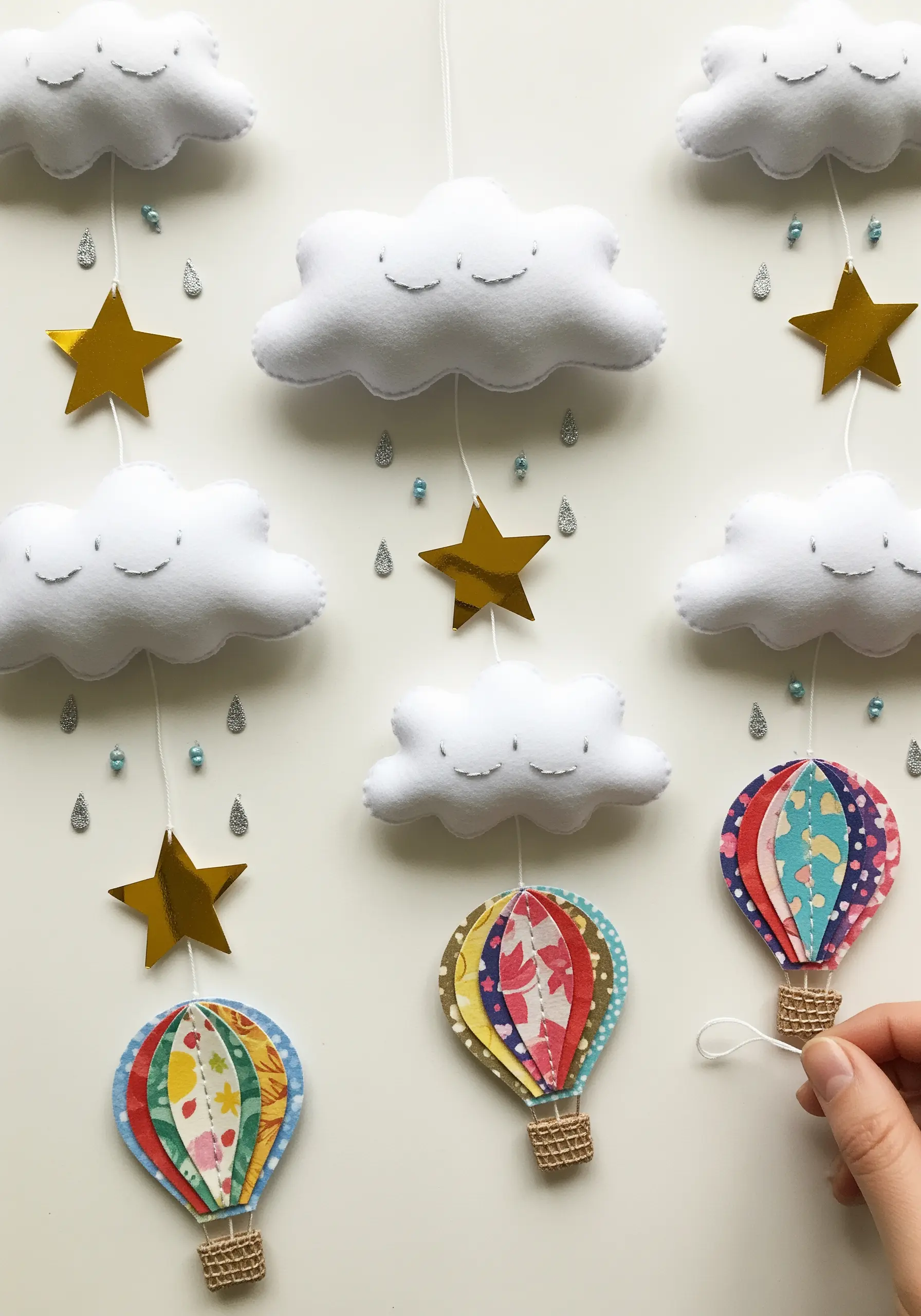 A nursery mobile with smiling, padded felt clouds and colorful paper hot air balloons.
