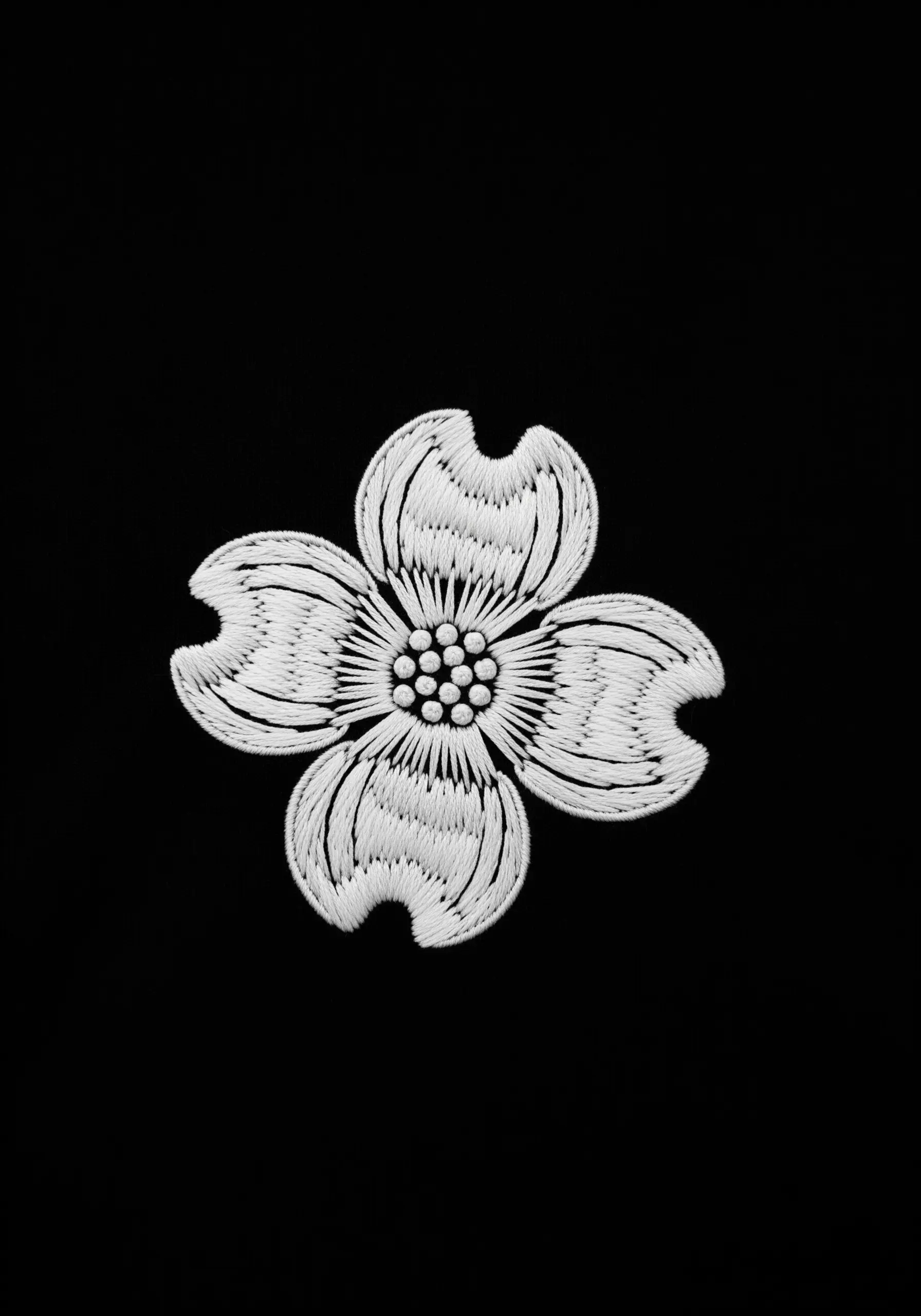 A detailed white dogwood flower with french knot center embroidered on black fabric.