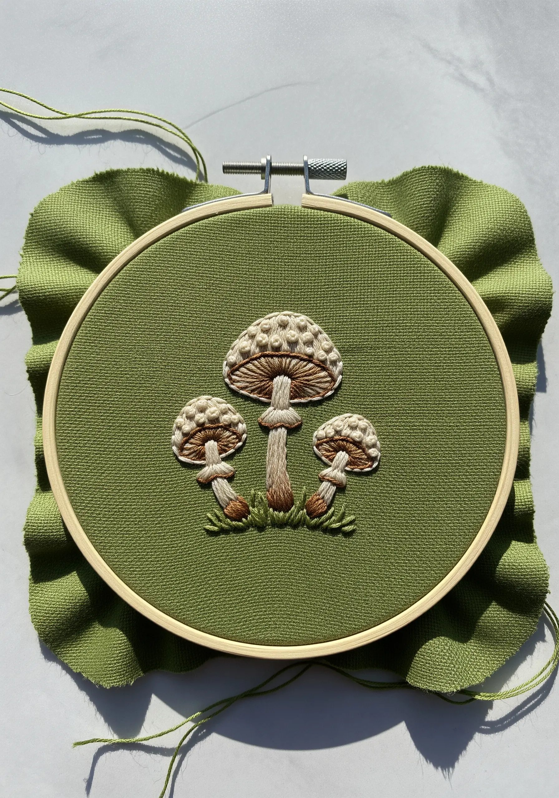 Three detailed mushrooms embroidered on green fabric, showing texture and shading.