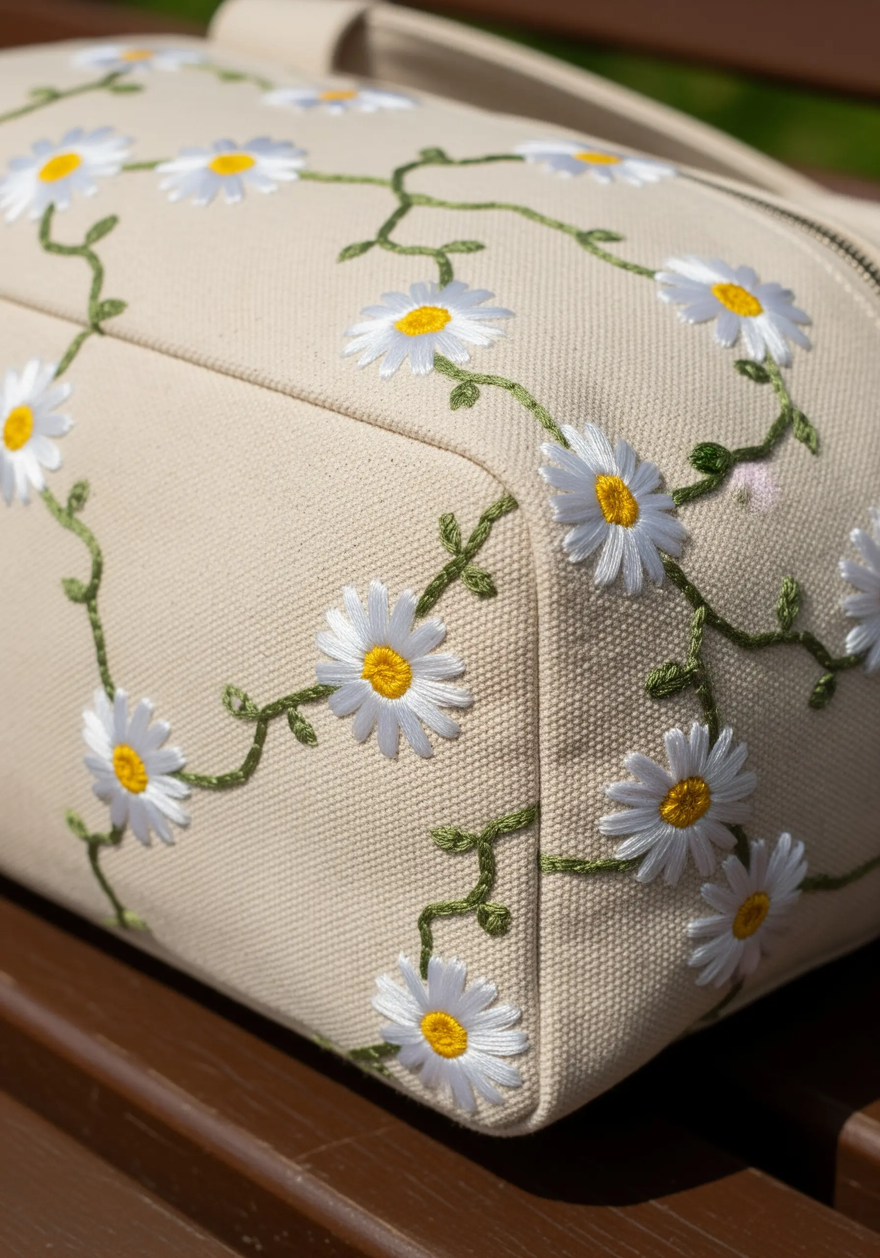 Embroidered daisies with green vines wrapping around the corner of a structured canvas bag.
