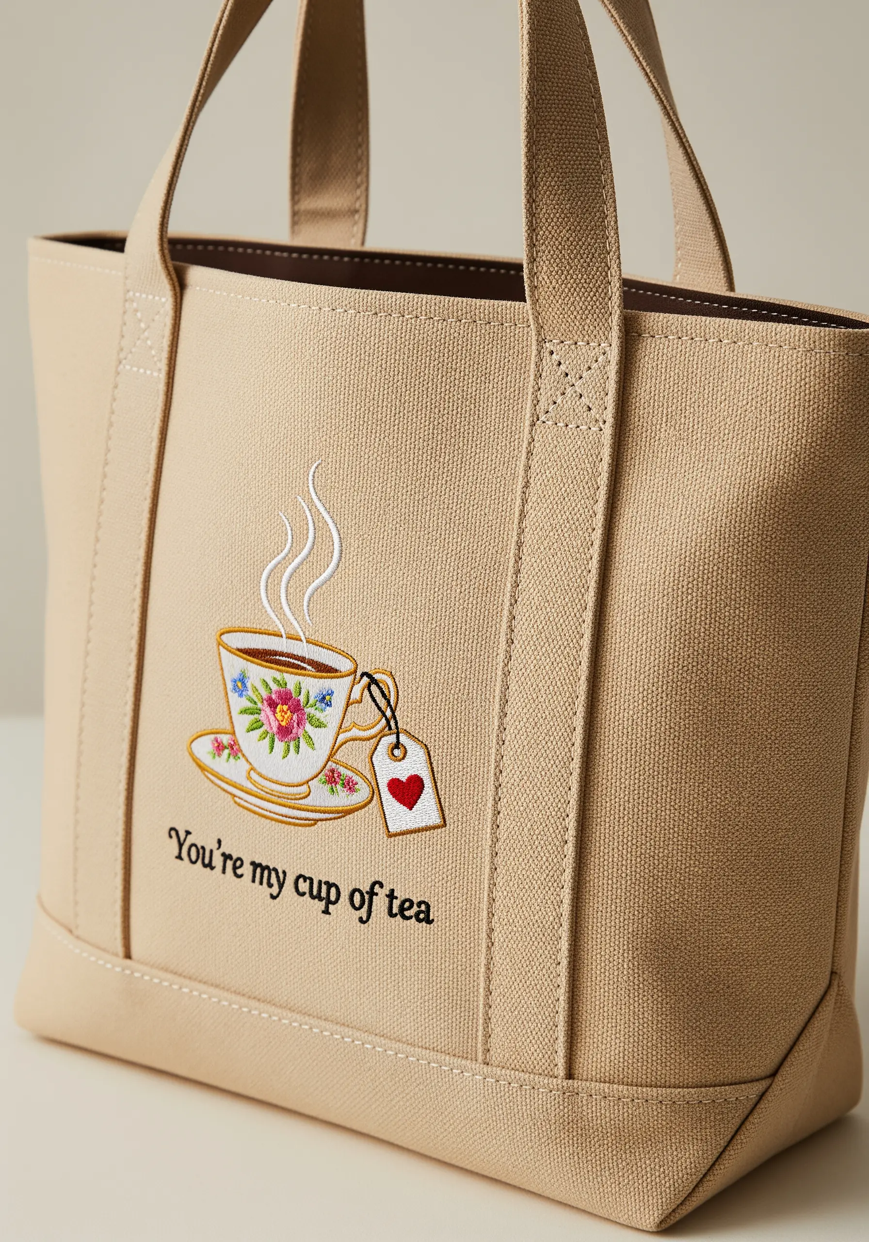 An embroidered teacup with a floral pattern and a tag that has a red heart, on a canvas tote.