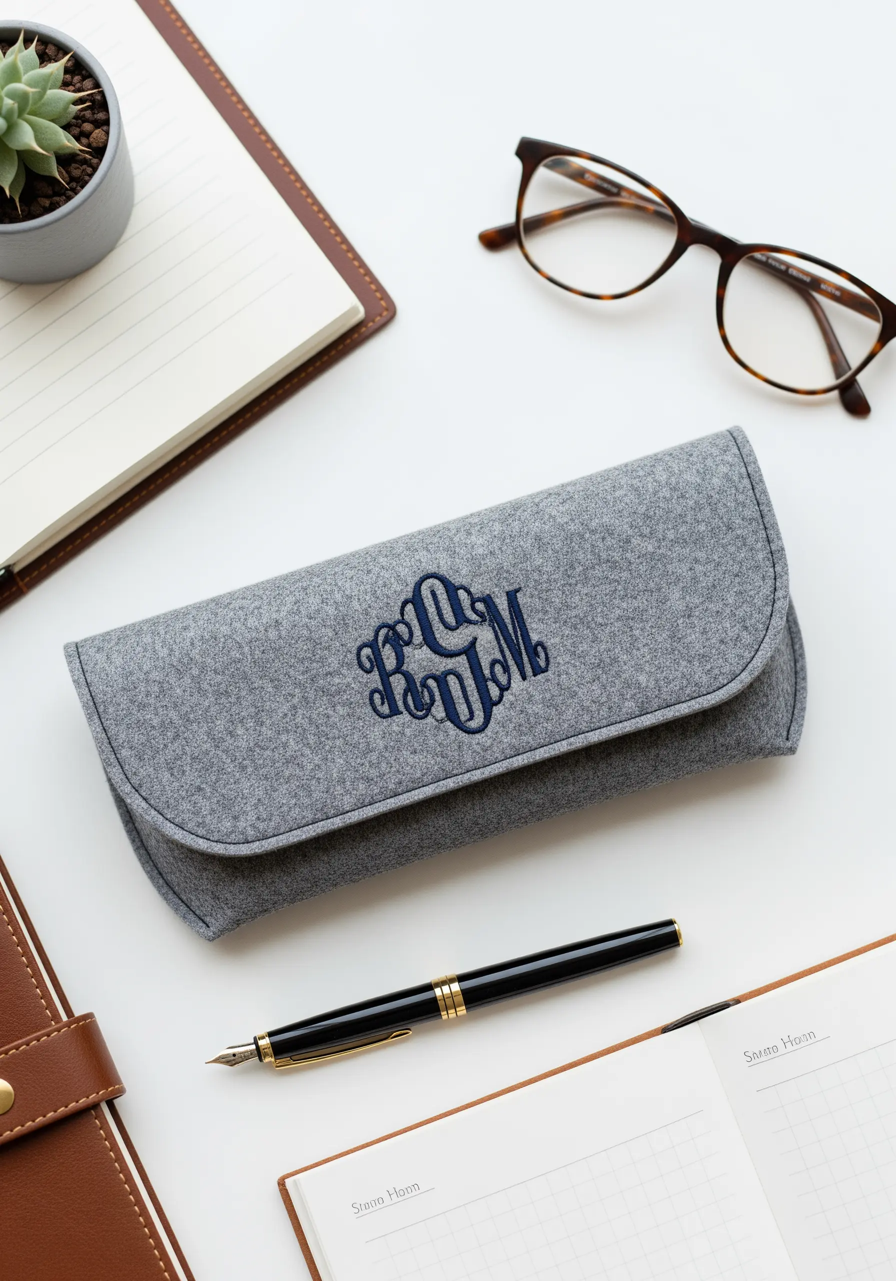 A gray felt glasses case with a detailed, navy blue interlocking monogram stitched on the front.