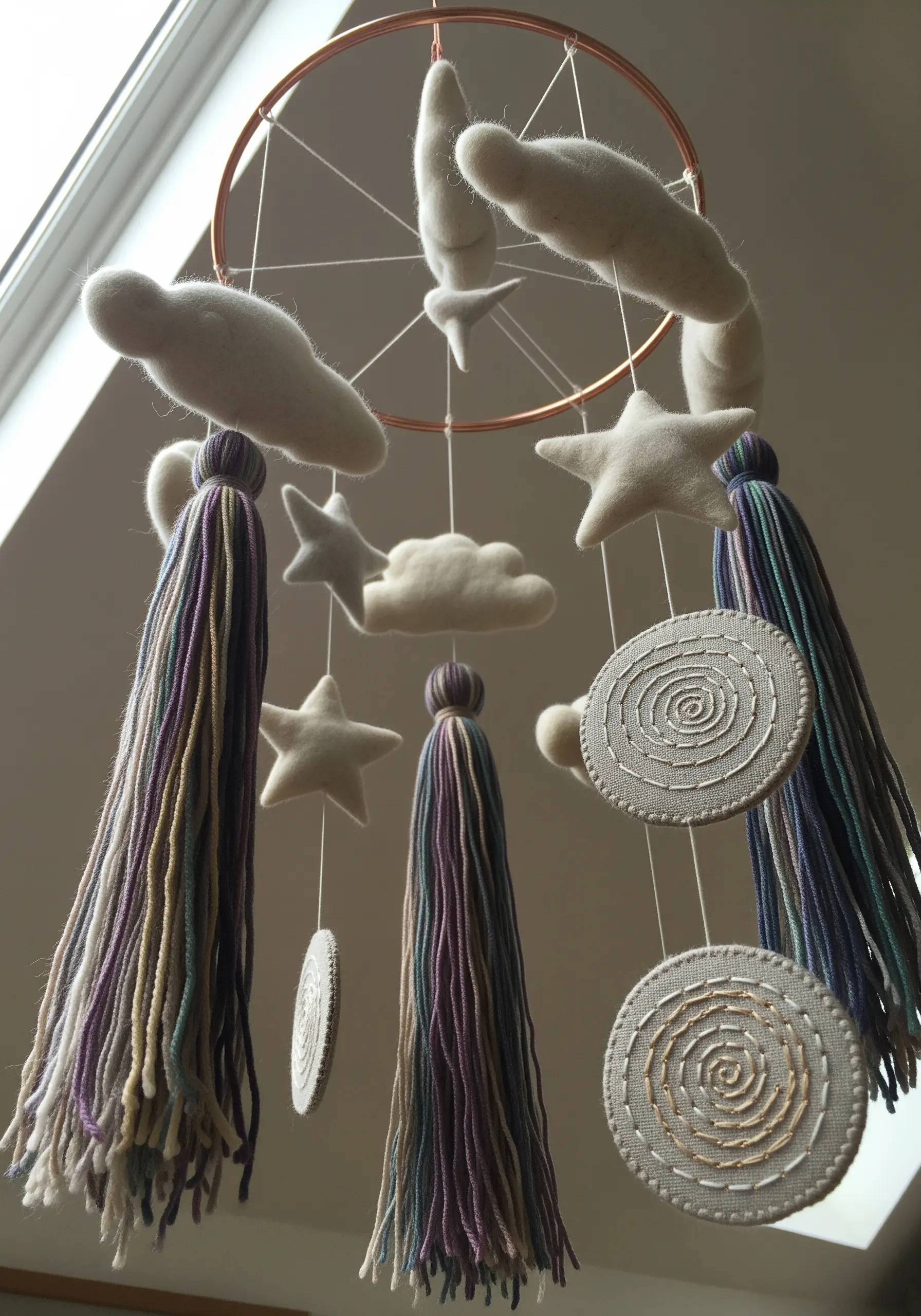 Nursery mobile with felted clouds, stars, embroidered discs, and long yarn tassels.