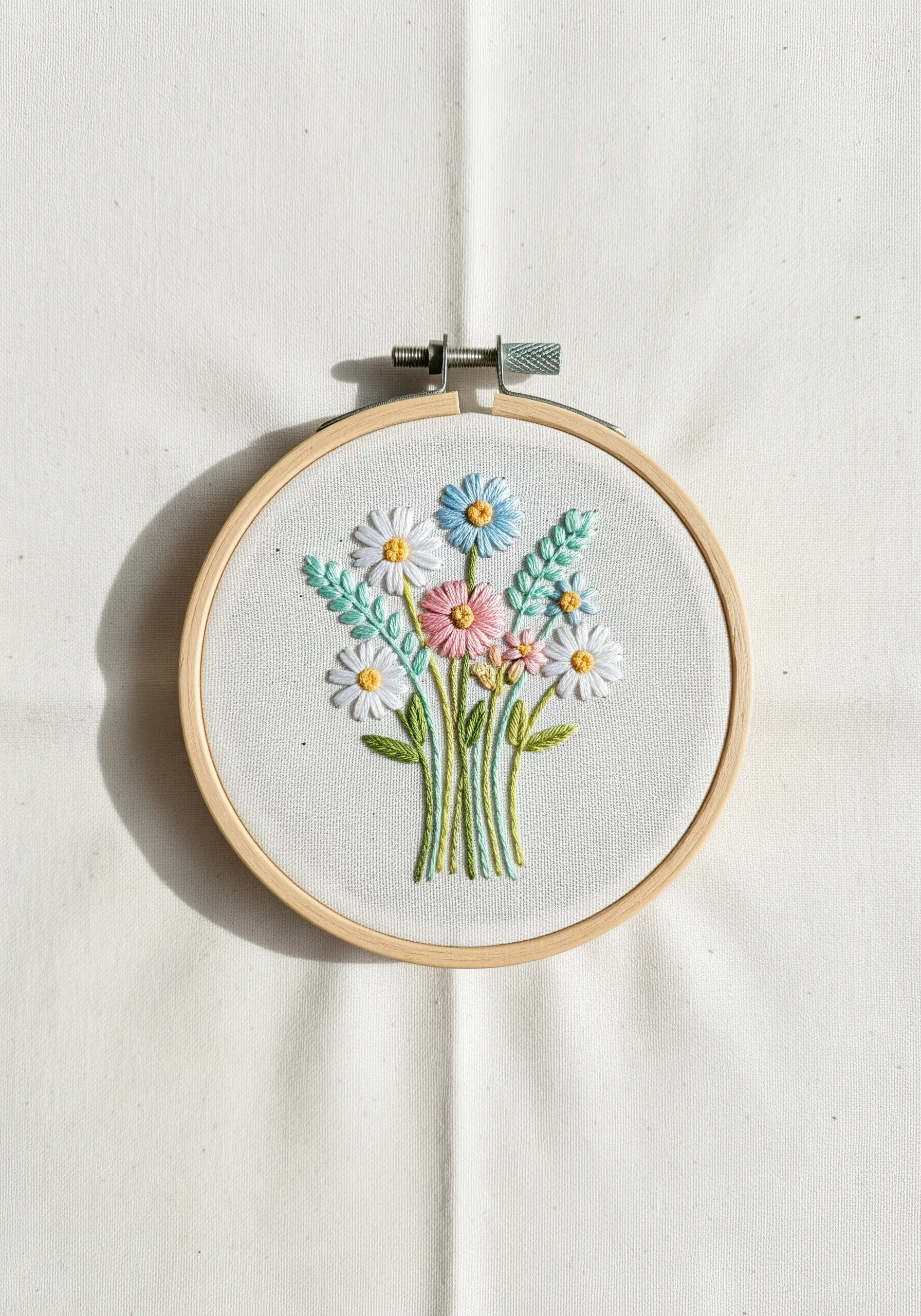 A vibrant bouquet of embroidered wildflowers with daisies, cosmos, and leaves in a hoop.