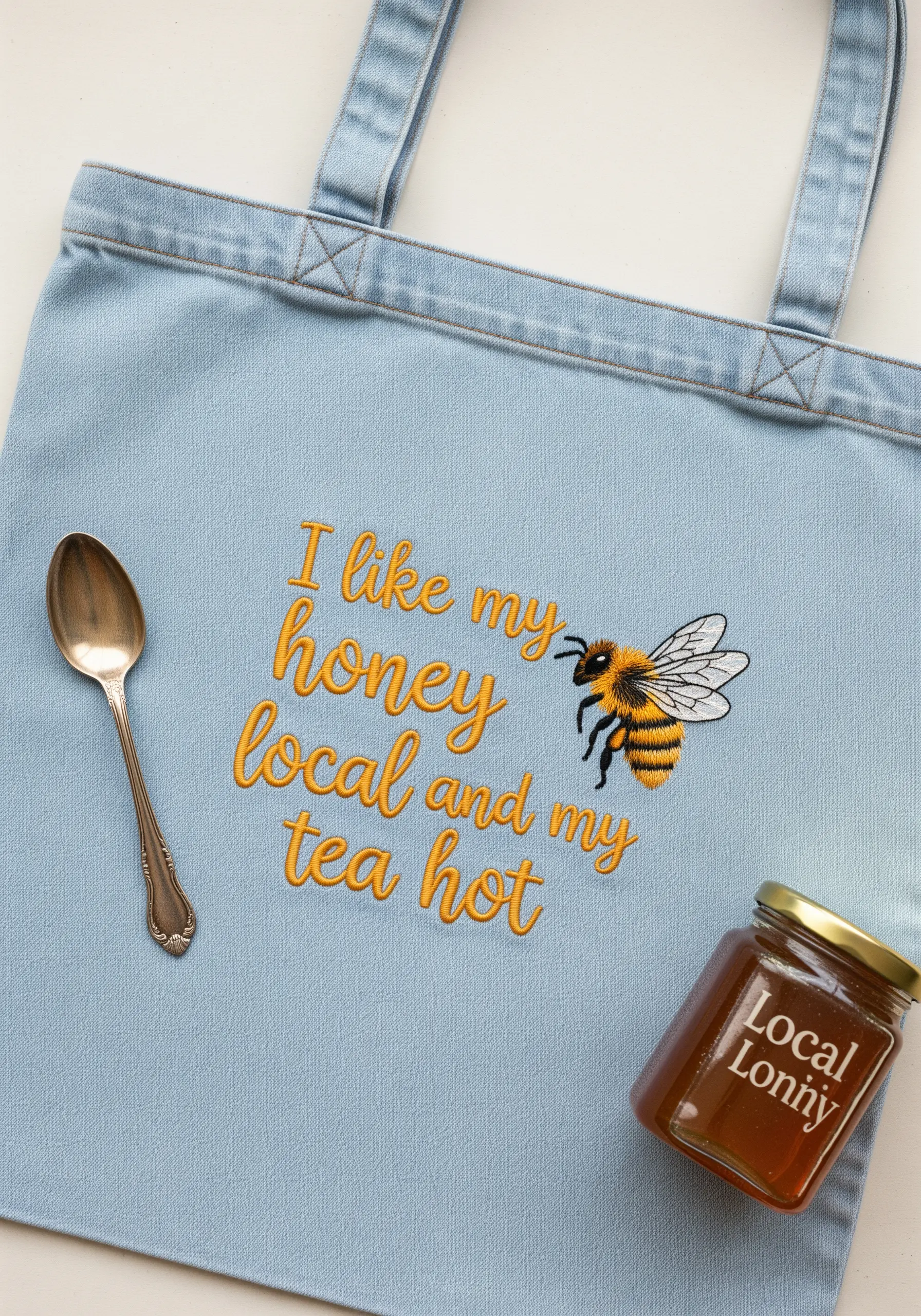 Embroidery on a light denim tote with a realistically stitched bee and yellow script.