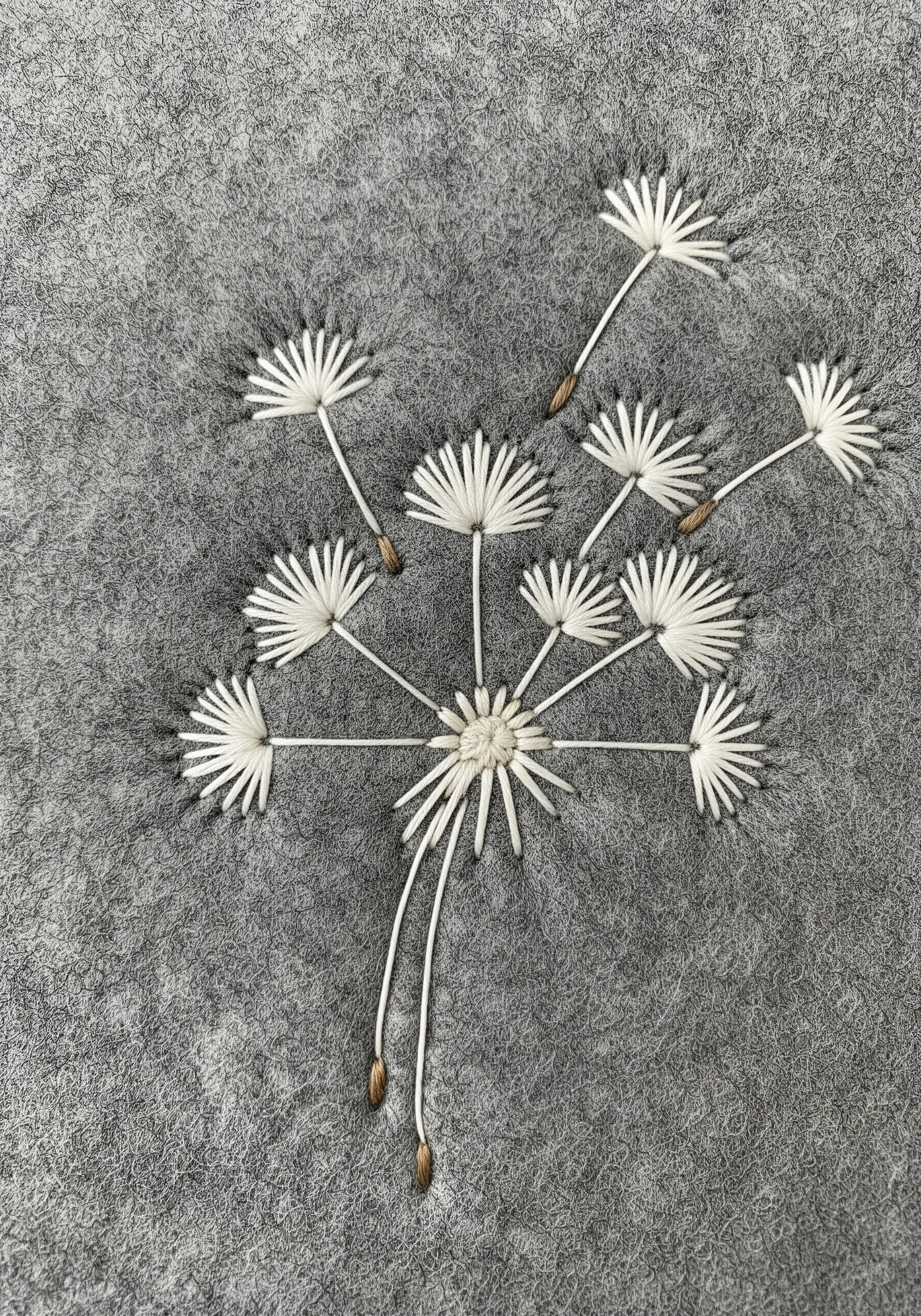 Delicate white dandelion seeds embroidered with straight stitches on grey felt fabric.