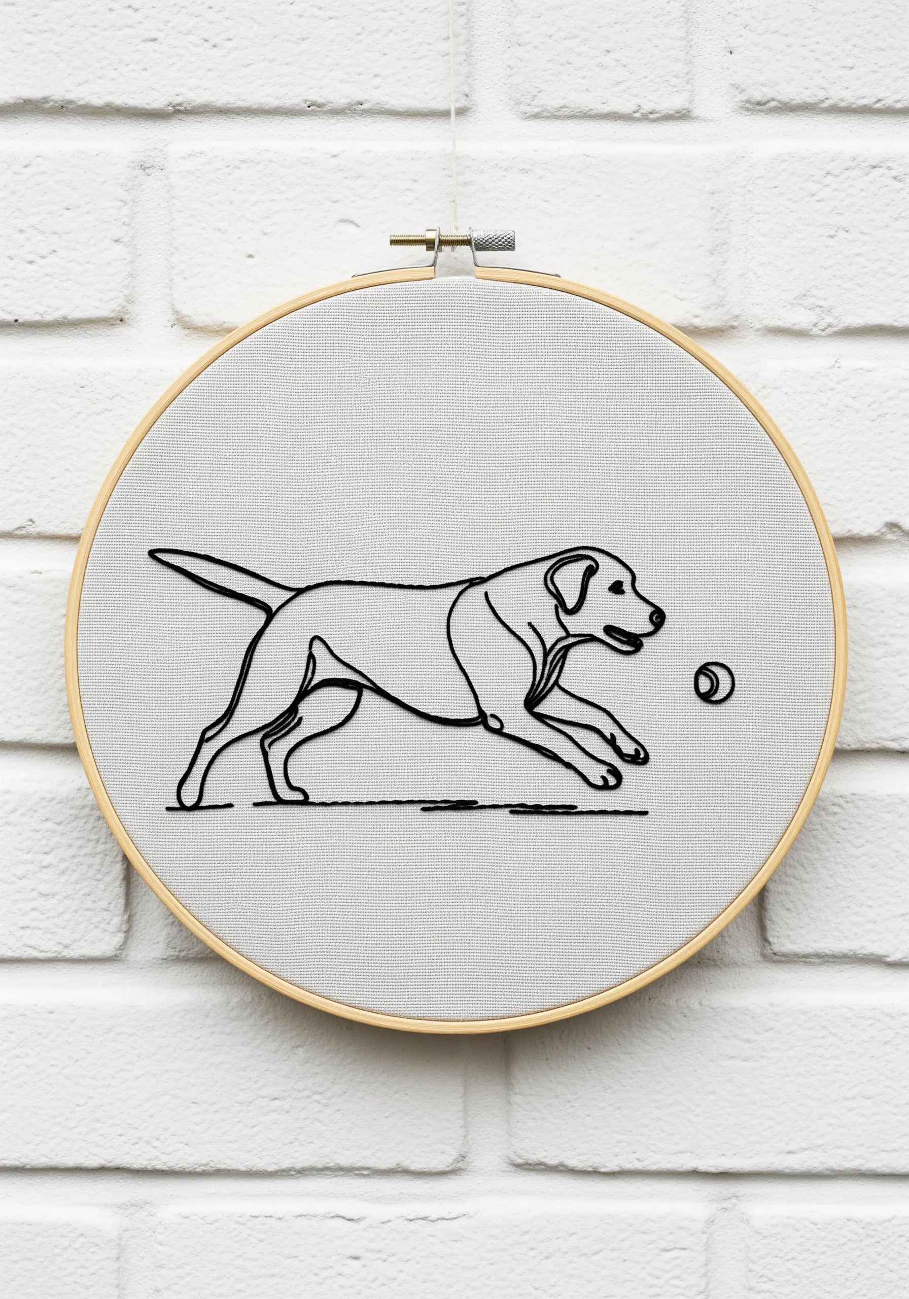 Minimalist line embroidery of a Labrador running towards a ball on a light grey background.