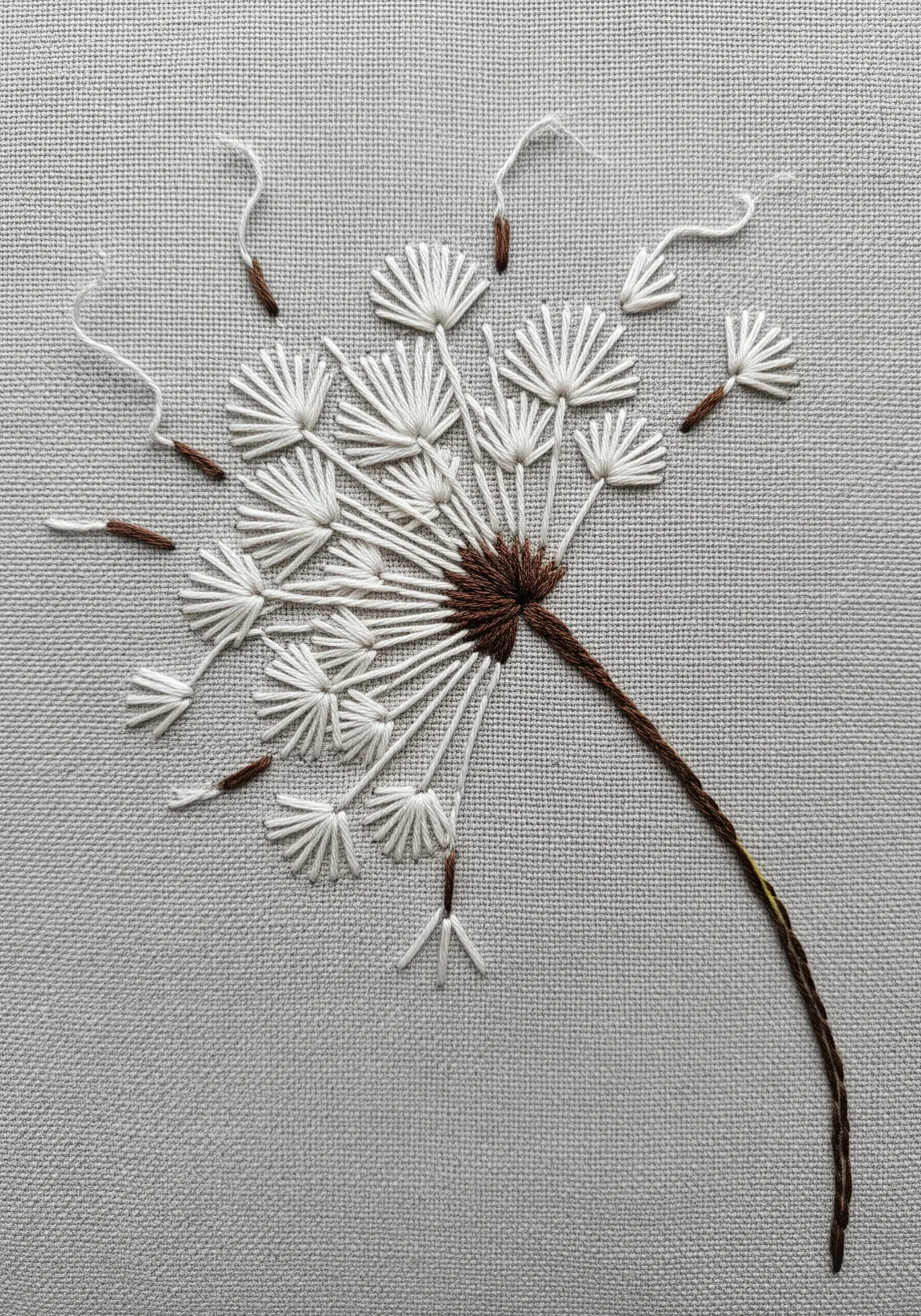 An embroidered dandelion head with white florets made from detached chain stitches.