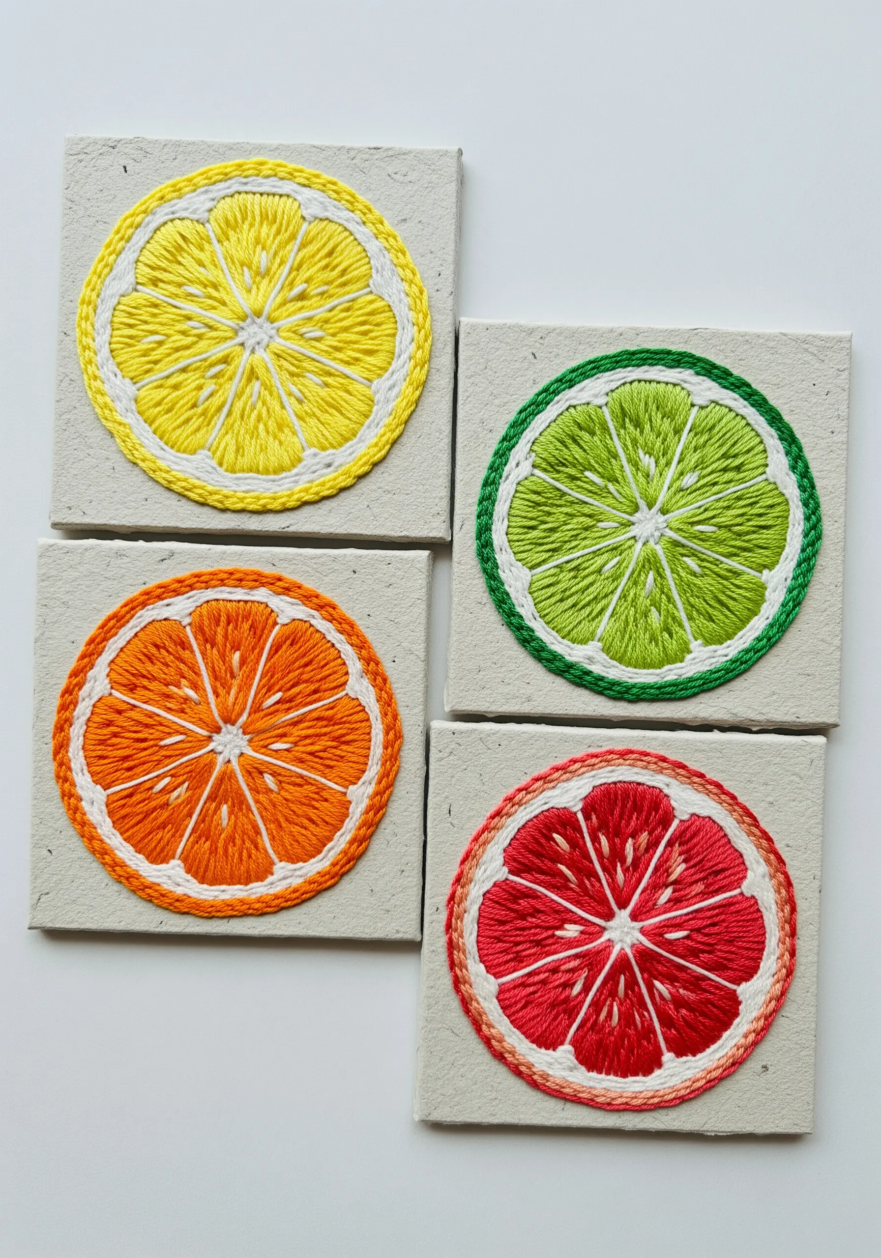 Four small canvases, each featuring a different embroidered citrus slice: lemon, lime, orange, and grapefruit.