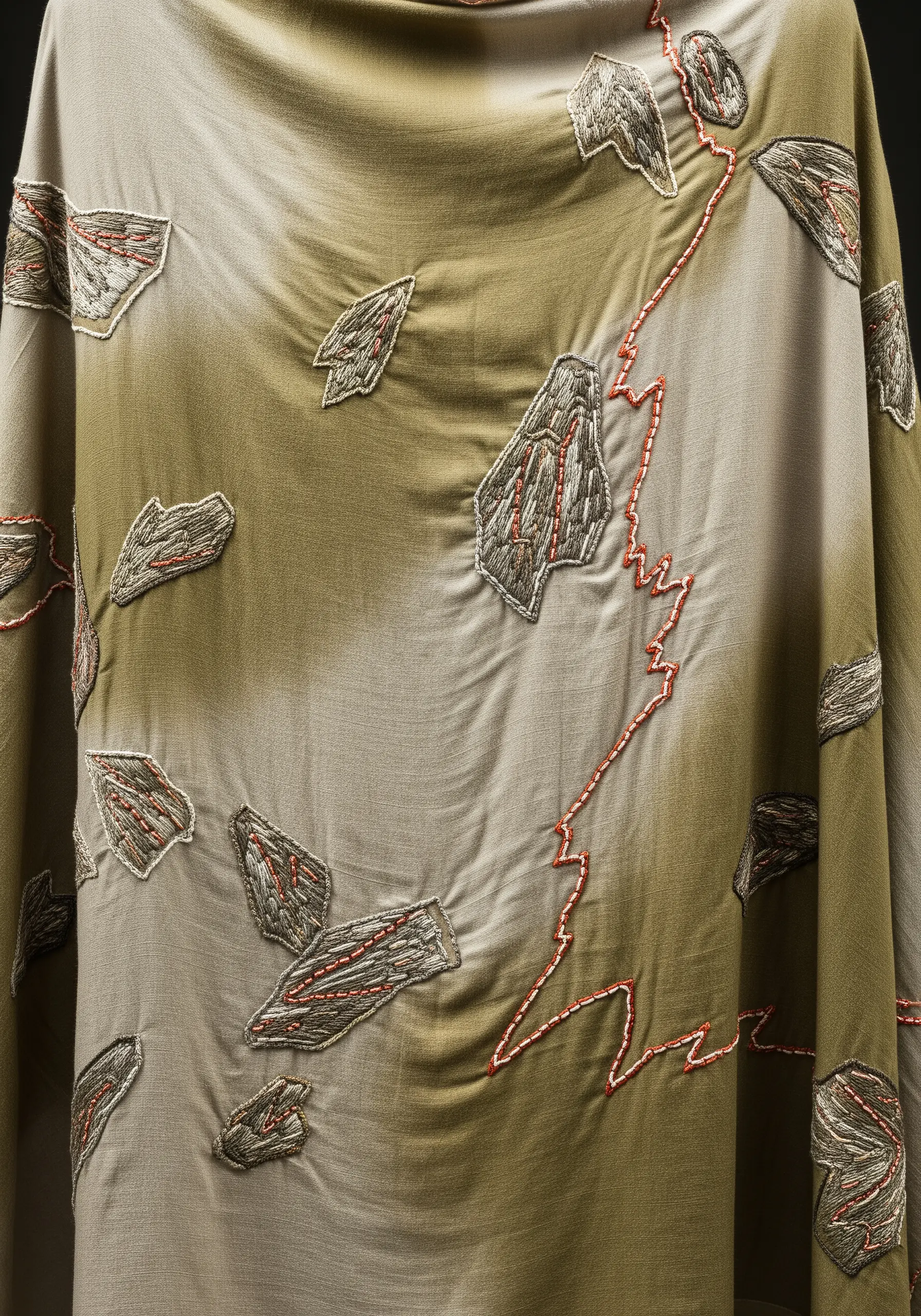 Abstract gray embroidered shapes on a tie-dyed green fabric, with a sharp red stitched line cutting through.