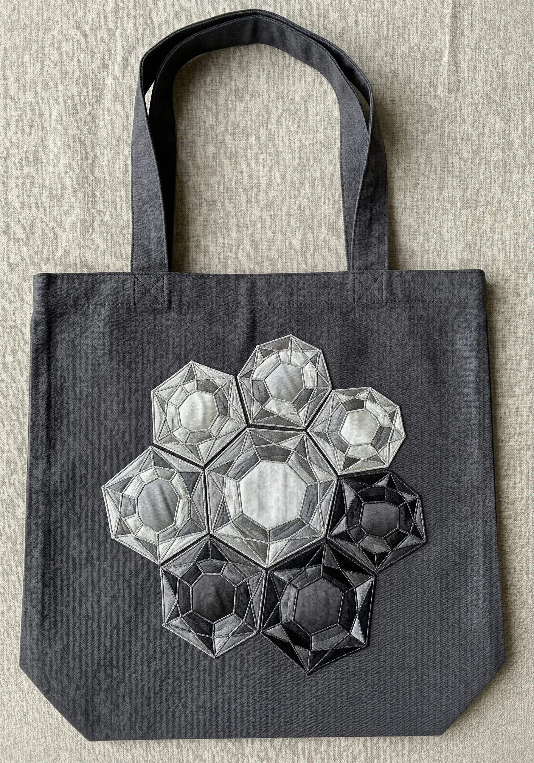 A cluster of geometric, crystal-like shapes in monochrome appliqué on a dark grey tote.