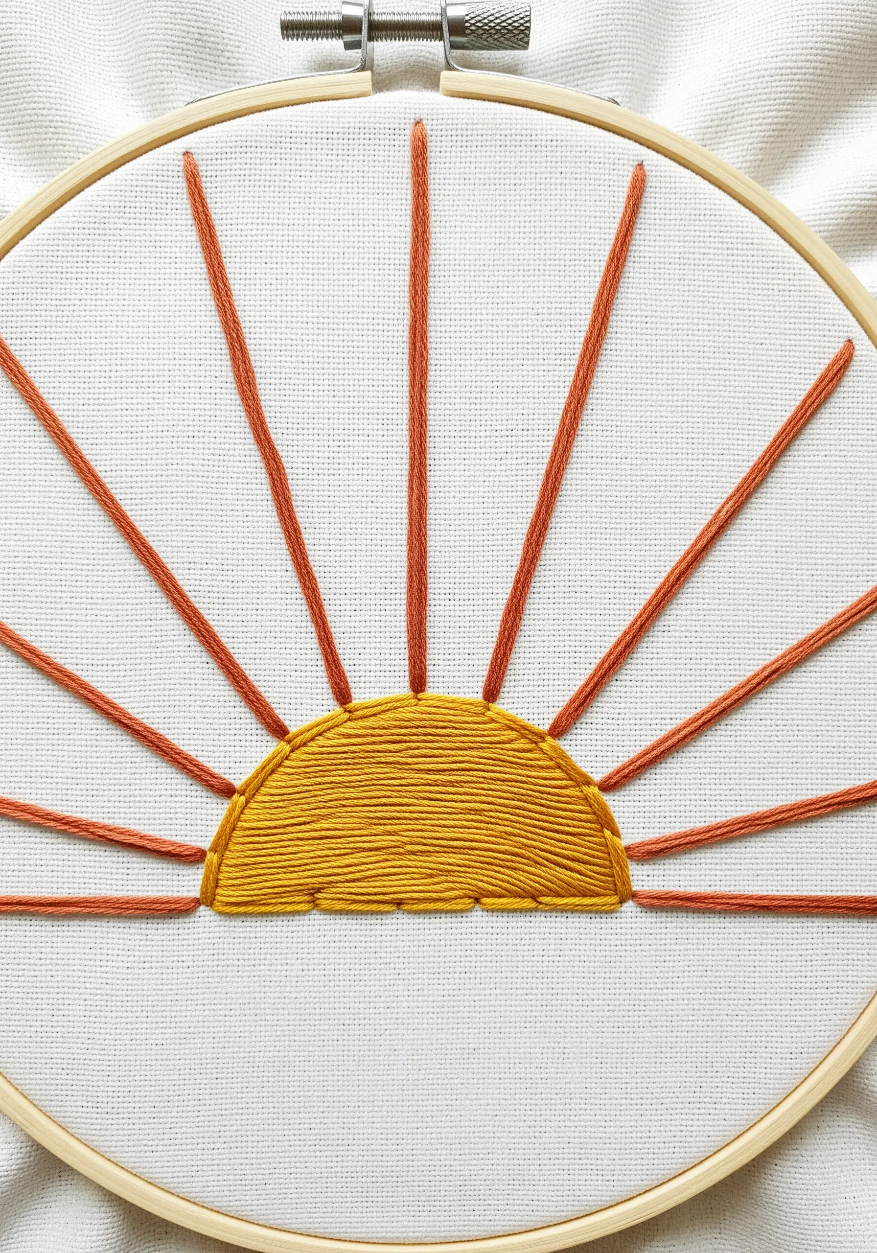 A minimalist embroidered sun with a satin-stitched semi-circle and long straight-stitch rays.
